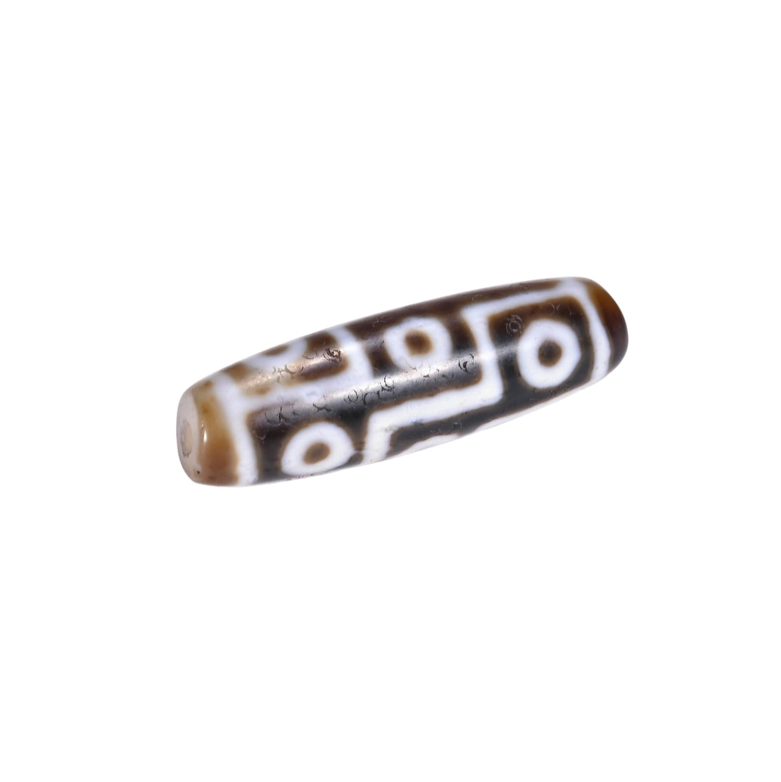 A CHINESE MULTI EYE DZI BEAD: Measuring 4.1 cm in length, this elongated cylindrical dzi bead is crafted from polished agate with warm translucent brown hues at both tapered extremities. Stark creamy-white etched geometric lines o
