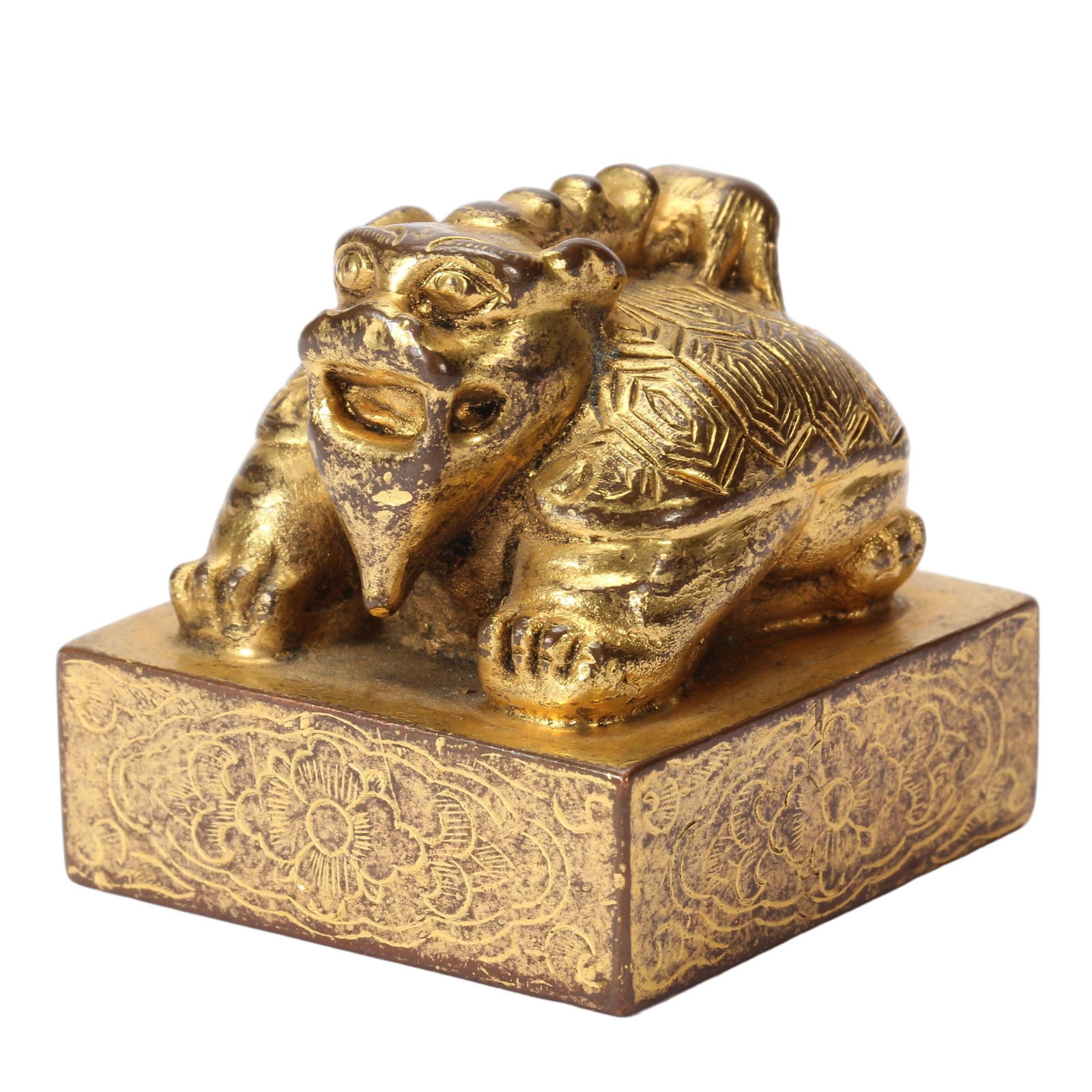 A CHINESE GILT BRONZE SEAL: This finely wrought square seal is topped by a crouching mythical beast knob with sharply rendered facial details and geometric engraved shell patterns across its back. The vertical sides of the block