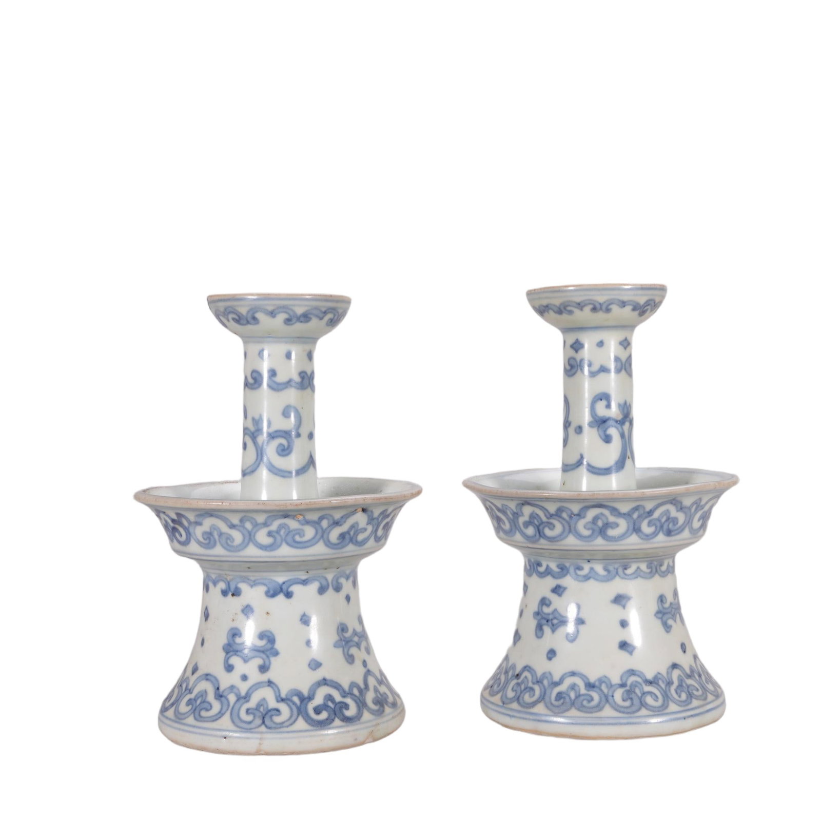 A PAIR OF CHINESE BLUE AND WHITE RUYI CANDLESTICKS: This matching pair of candlesticks is structured with a flared stepped base, wide drip tray and slender central stem capped by a small candle holder. The entire surface is decorated with fluid undergl