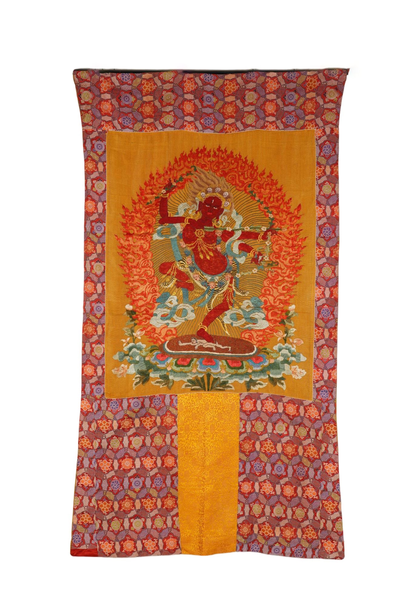 A CHINESE EMBROIDERED VAJRAVARAHI THANGKA: Measuring 79 x 100 cm, this intricately stitched thangka centres upon vivid red-hued Vajravarahi dynamically posed atop a decorated lotus pedestal. The deity is encircled by blazing embroidered flame 