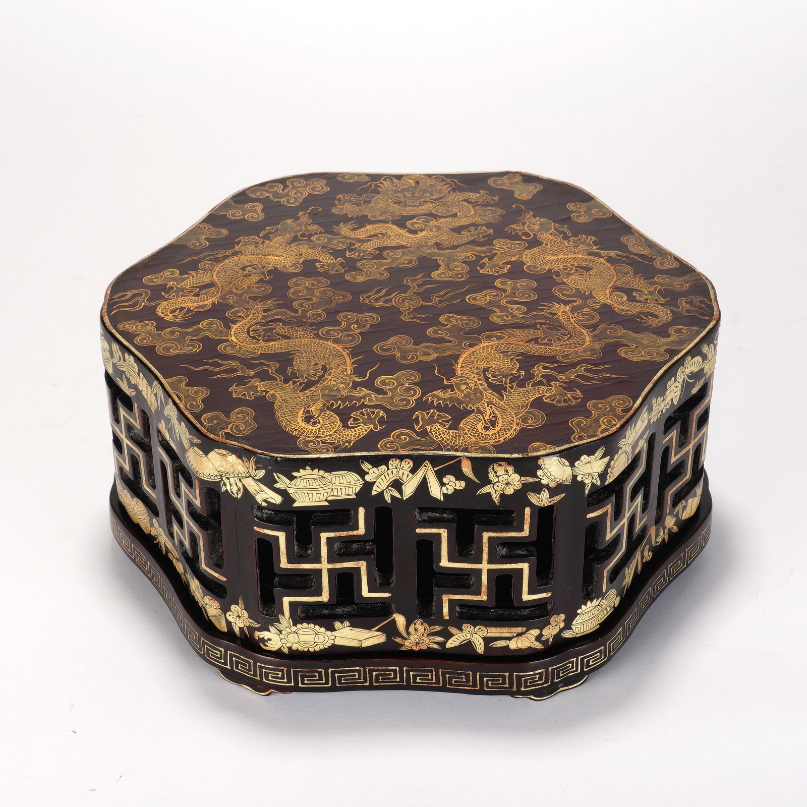 A CHINESE GILT DECORATED LACQUER DRAGON BOX: This handsome multi-sided lacquer box features a deep polished dark lacquer ground enriched by lavish gilded ornamentation. Its domed lid is adorned with vivid gilt dragons winding across swirling clo