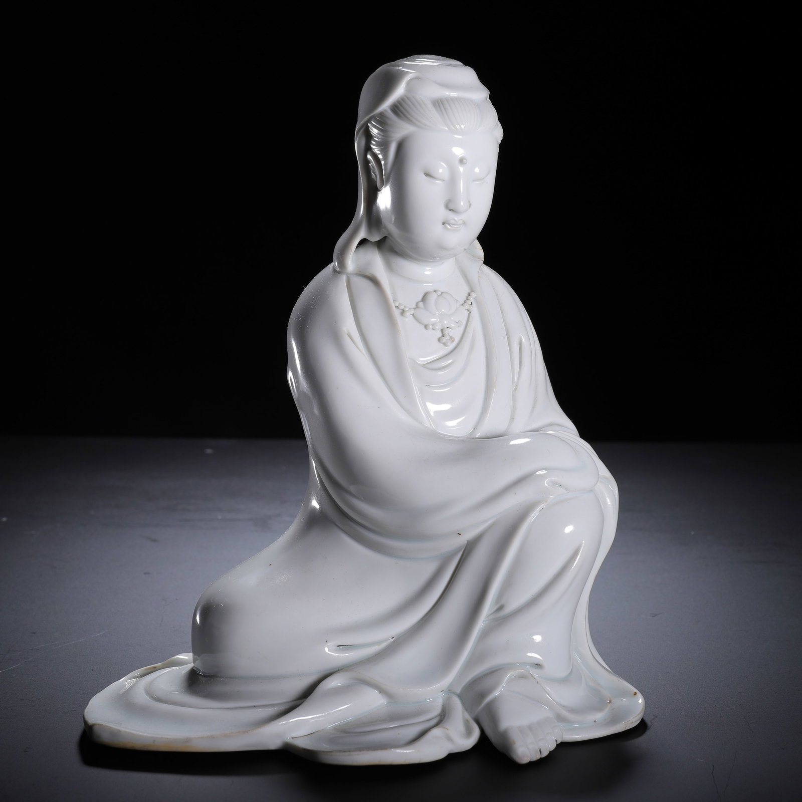 A CHINESE DEHUA WHITE PORCELAIN GUANYIN: Weighing 970 grams, this serene porcelain figure measures 16 cm long, 12 cm wide and 19 cm in height. Rendered in iconic Dehua creamy ivory glaze with a silky glossy finish, Guanyin rests in an elegan