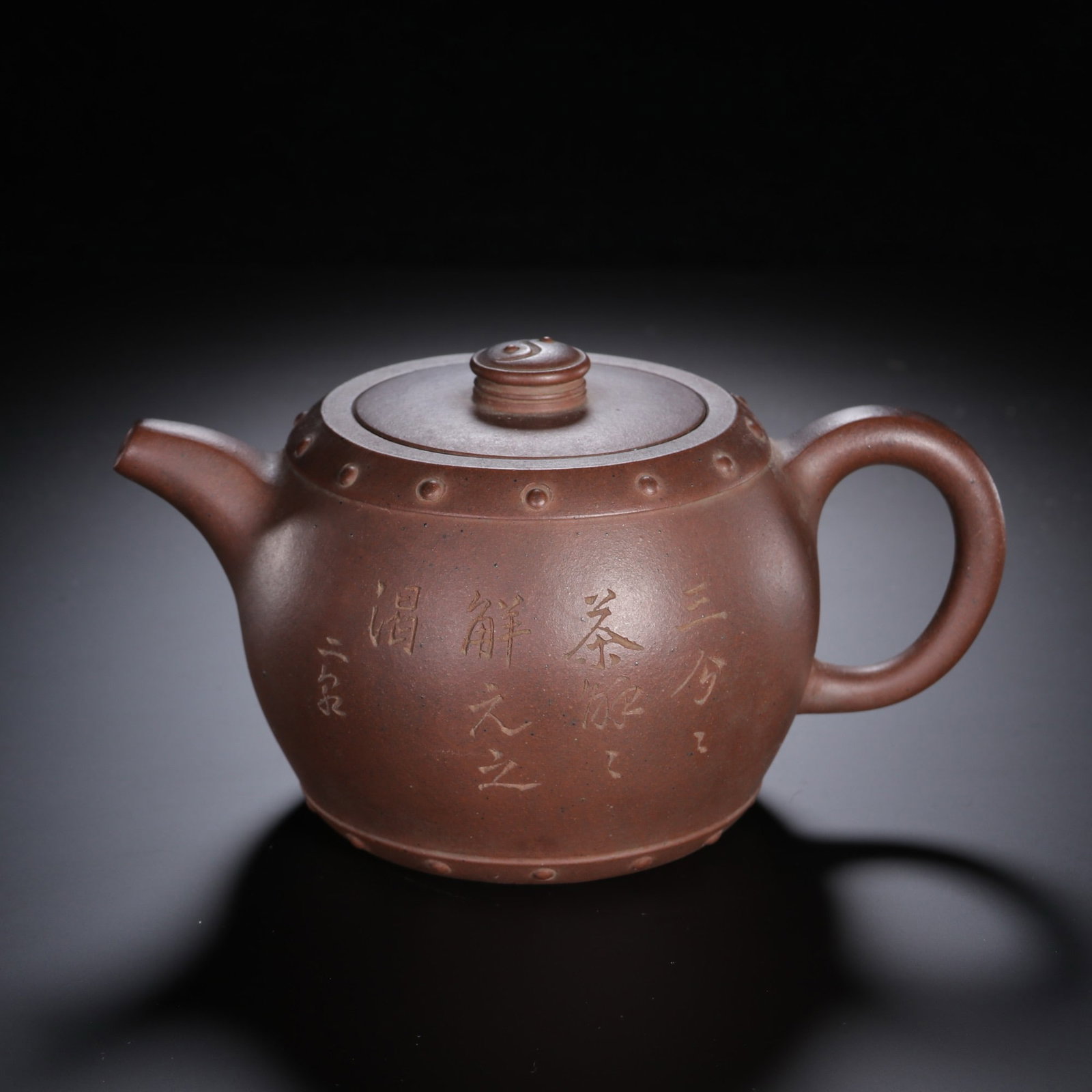 A CHINESE DRUM STUD INSCRIBED ZISHA TEAPOT: Standing 10.5 cm tall with a width of 18 cm, this stout-bodied teapot is fashioned from rich earth-toned Yixing zisha clay with a smooth matte finish. Rows of raised drum-like studs neatly line the li