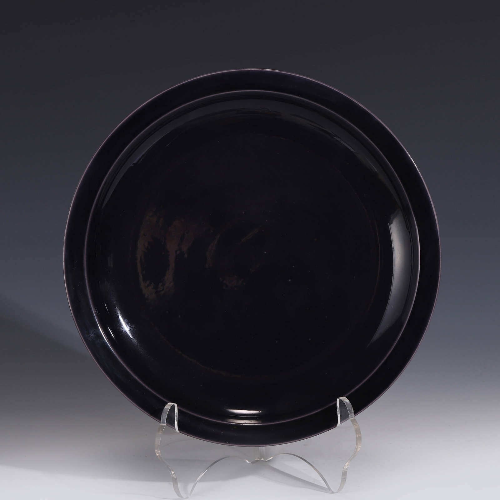 KANGXI EGGPLANT PURPLE GLAZED PLATE: Dimensons: Measurements: Height: 4 cm Diam: 28 cm Chinese Qing Dynasty Period, Kangxi Eggplant Purple Glazed Porcelain Plate. The plate has a broad wide central interior, rounded mouth rim, raised on 