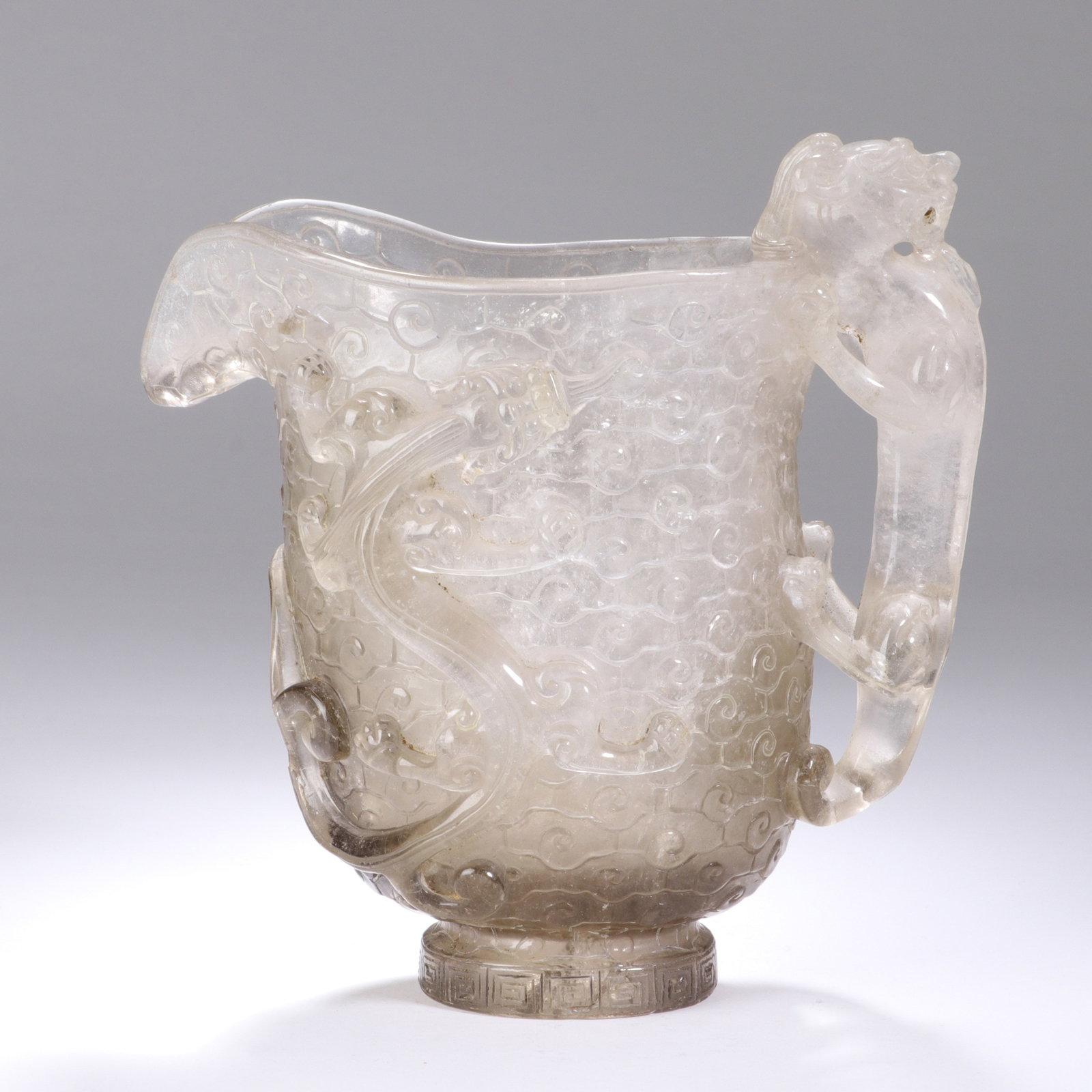 A CHINESE CRYSTAL DRAGON MOTIF CUP: Standing 14 cm in height and spanning 15 cm in width, this superb vessel is hewn from translucent rock crystal carrying faint natural veining that lends subtle depth to its polished facade. A sculpted