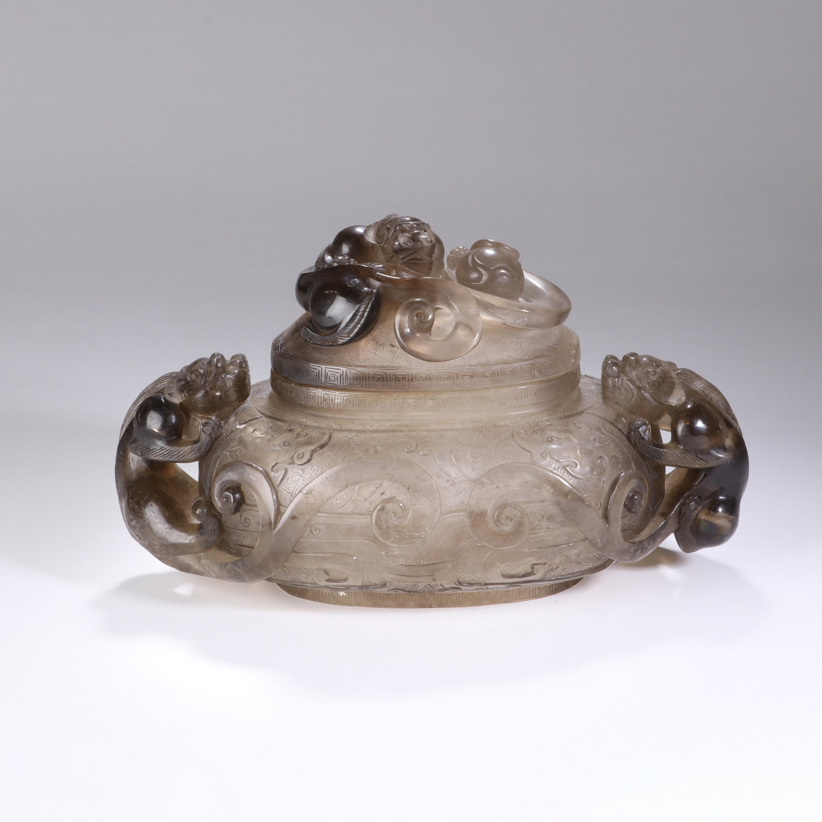A CHINESE CRYSTAL DRAGON PATTERN CENSER: Measuring 16 cm both in height and width, this stout-bodied censer is meticulously carved from smoky crystal marked by natural tonal gradients that deepen around sculpted dragon features. A curled myt
