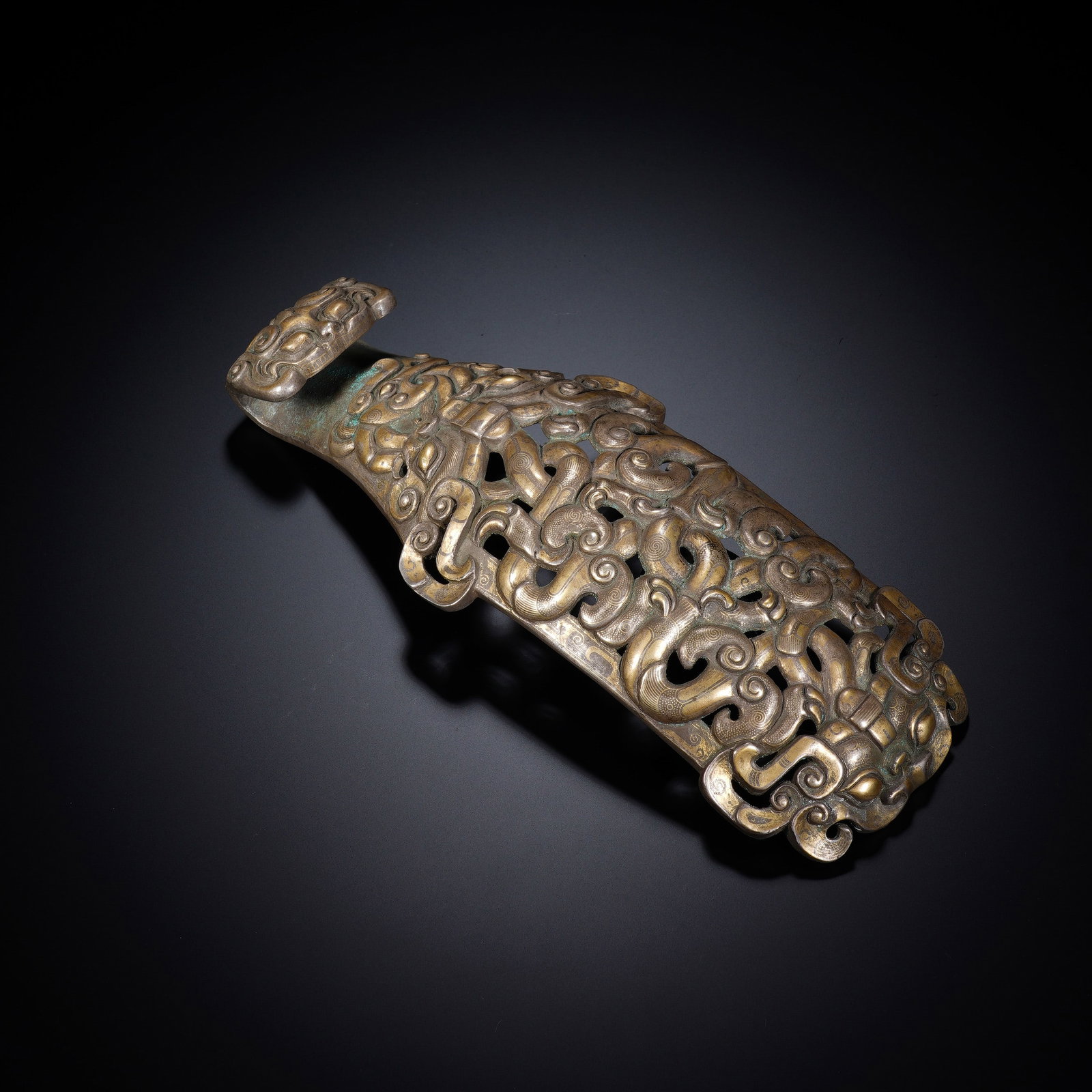 A CHINESE BRONZE BELT HOOK: Crafted from aged bronze, this substantial belt hook boasts elaborate openwork carving across its elongated body. Intertwined scrolling mythical beast motifs wind intricately throughout the pierced de