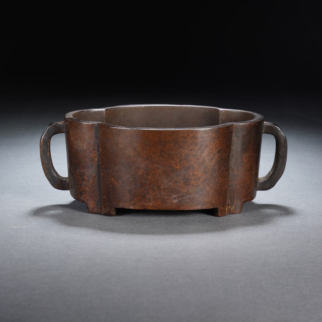 A CHINESE TWIN HANDLED BRONZE CENSER: Crafted from dense cast bronze, this low-profile censer features an elegant foliated lobed body with two symmetric curved loop handles extending outward from its sides. Short, neatly formed bracket fe