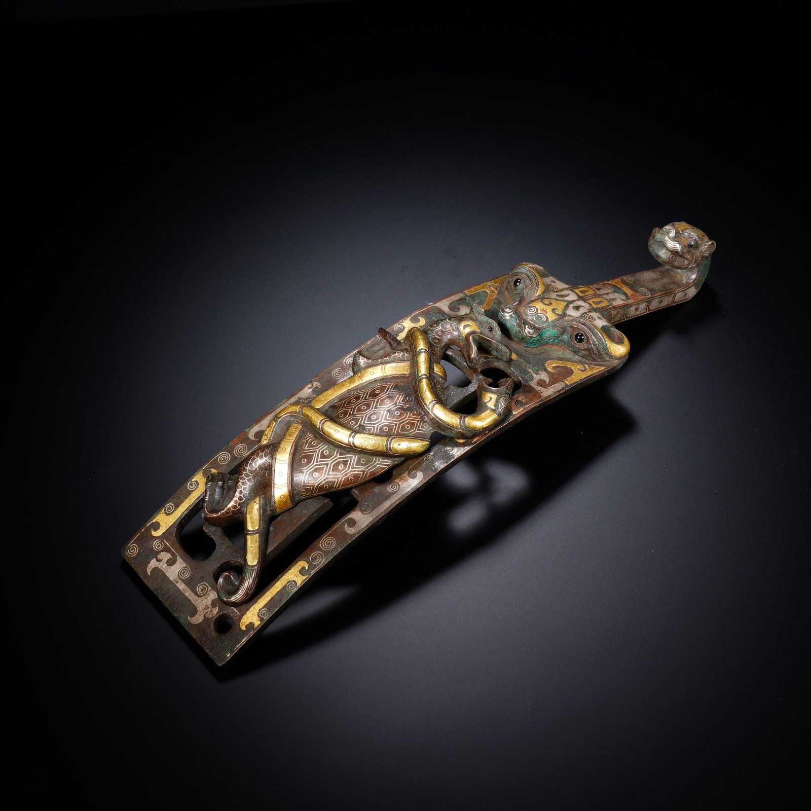 A CHINESE GOLD INLAID BRONZE BELT HOOK: This elaborate bronze belt hook showcases exquisite traditional gold and silver inlay craftsmanship across its curved body. Its terminal is sculpted into a refined mythical beast head, while the main 