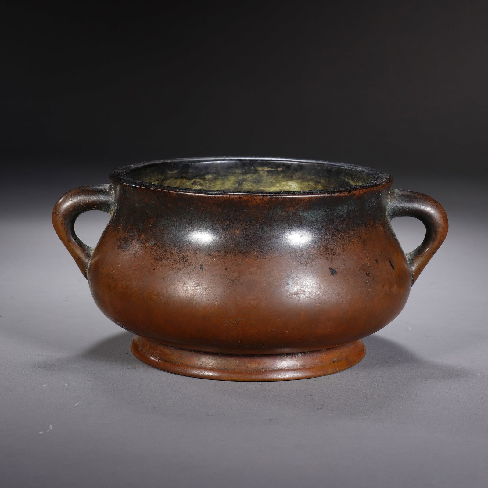 A CHINESE PLAIN PURPLE BRONZE EARED CENSER: Crafted from fine purple bronze, this minimalist censer features a smoothly bulging body flanked by a pair of elegant coiled dragon-style handles, sitting atop a neatly raised circular foot ring. Its 