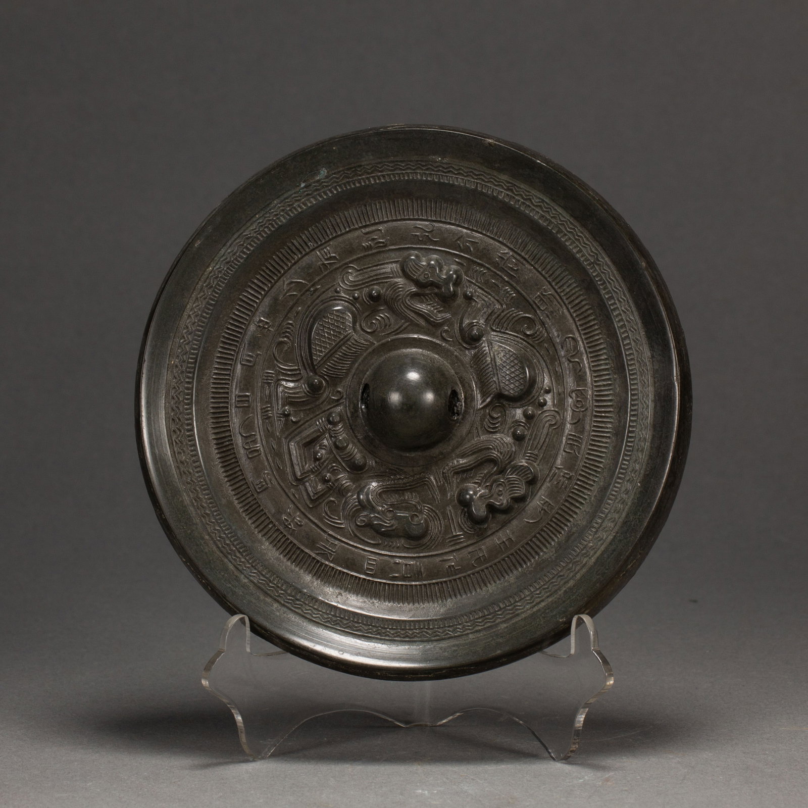 A CHINESE ARCHAIC BRONZE MIRROR: Measuring 13 cm both in length and width and weighing 710 grams, this circular bronze mirror features a polished raised central knob designed for convenient handling. Intricate relief carvings of swir