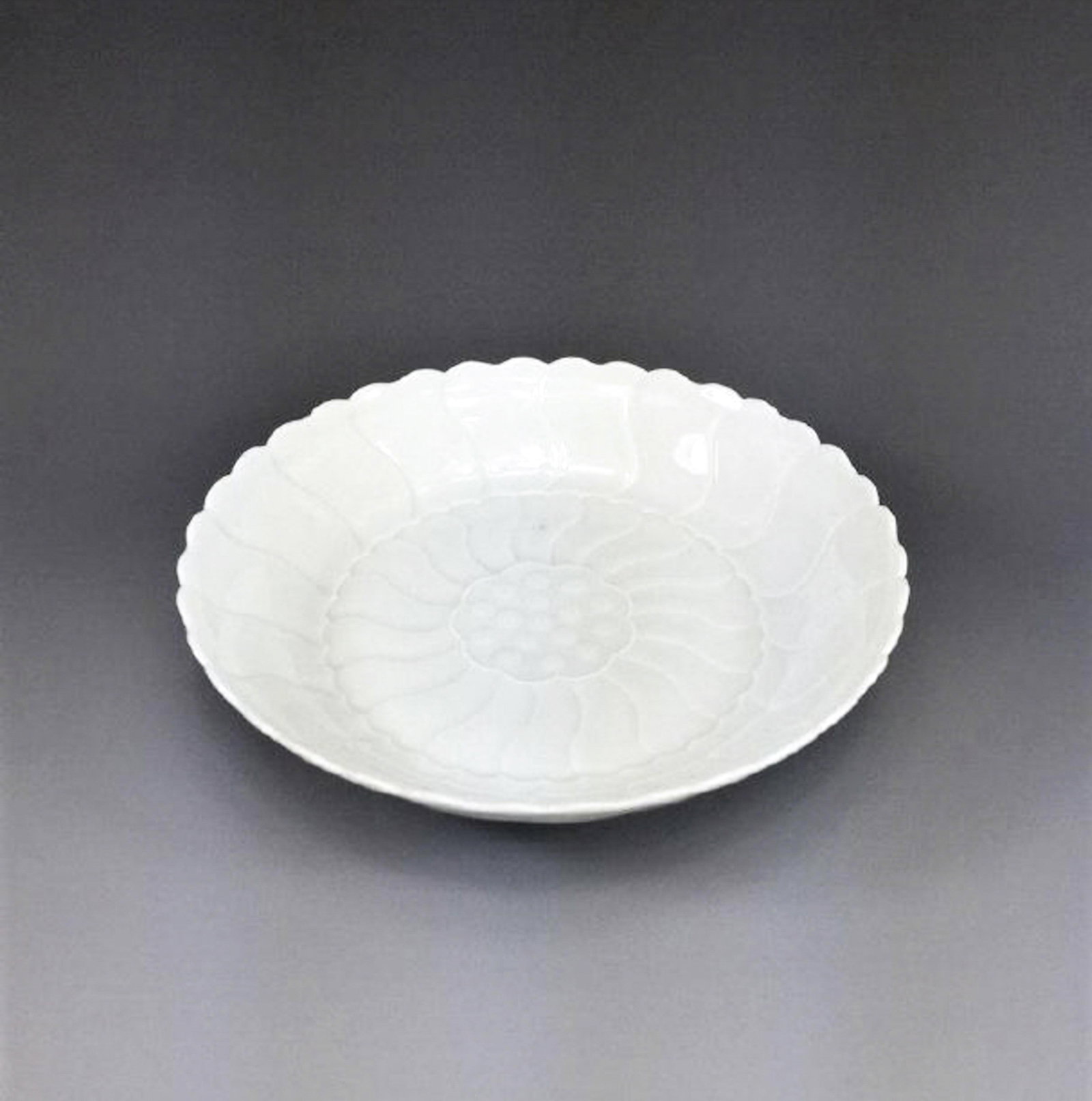 FINE CARVED FLORIFORM QINGBAI FLORAL DISH: Dimensions: 1-1/8" H x 5-1/8" Diam. Fine Chinese Qingbai porcelain dish The dish is shallow in design with a scalloped rim. The interior is shaped in a flori-form petal spanning out too the edge. crea