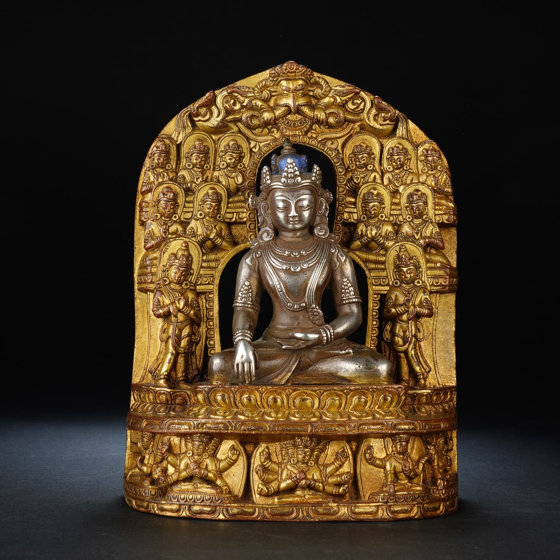 A CHINESE SILVER BUDDHA WITH GILT COPPER MANDORLA: Measuring 13 x 7 x 17 cm and weighing 1369 grams, this elaborate devotional statue features a primary Buddha cast in polished silver seated in serene meditation pose. The main figure is adorned with f