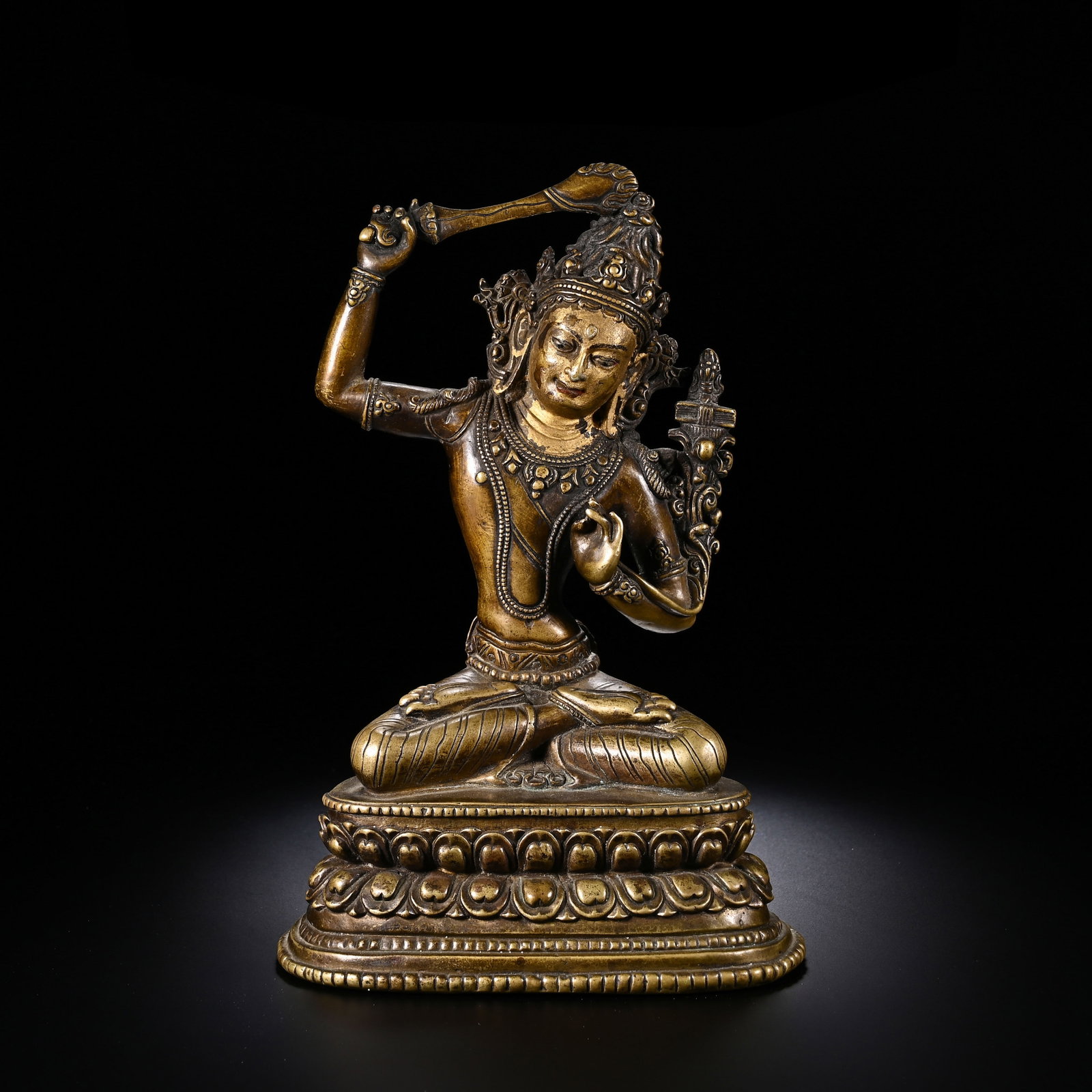 A CHINESE GILT BRONZE BUDDHA STATUE: Standing 18 cm tall and 12 cm across, this intricately cast Manjushri depiction settles in refined cross-legged lotus seating on a layered lotus pedestal edged with neat beaded mouldings. The deity sp