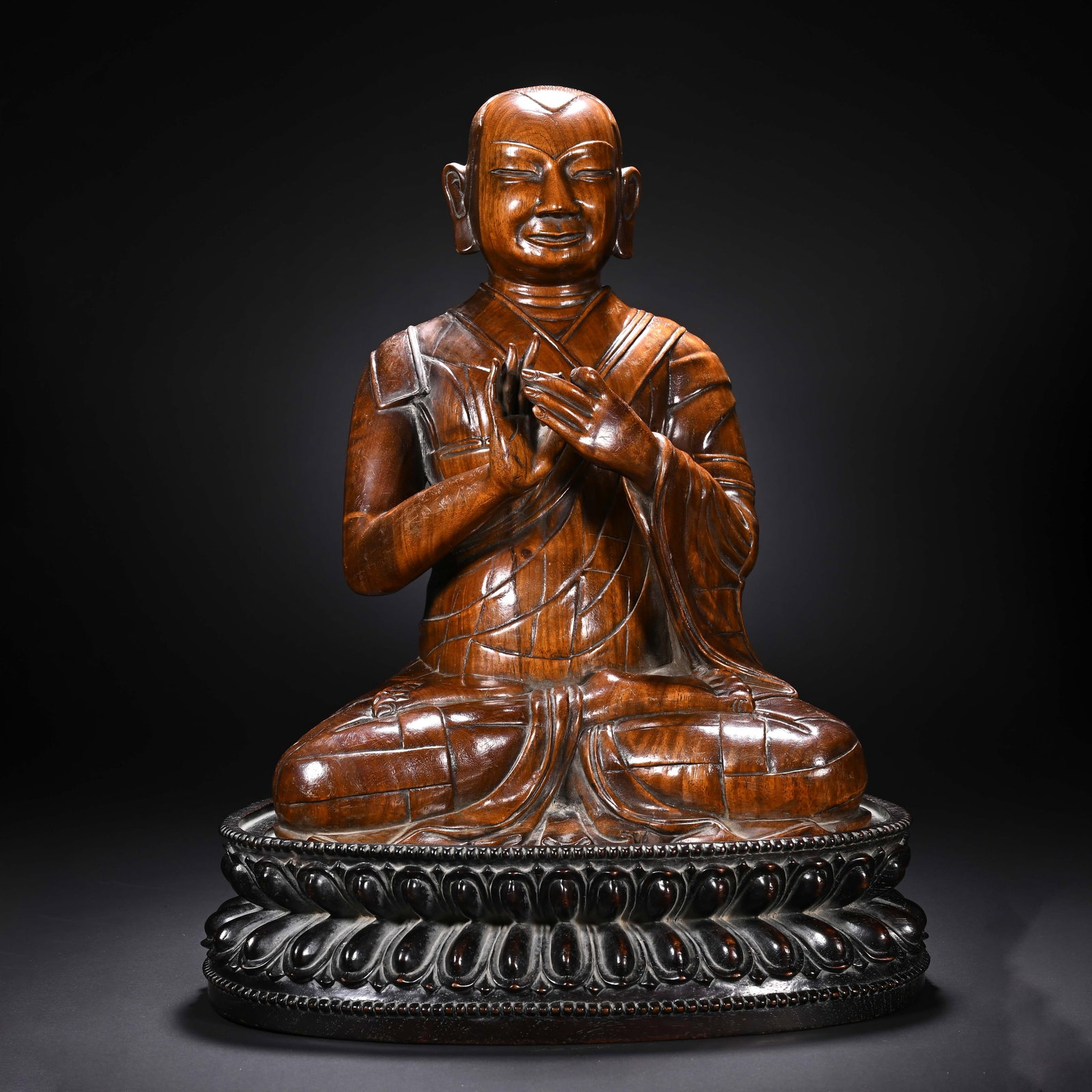 A CHINESE HUANGHUALI LUOHAN SCULPTURE: Standing 42 cm tall with a width of 31 cm, this refined carving depicts a seated luohan meticulously sculpted from premium huanghuali timber showcasing warm, flowing natural grain across its polished 