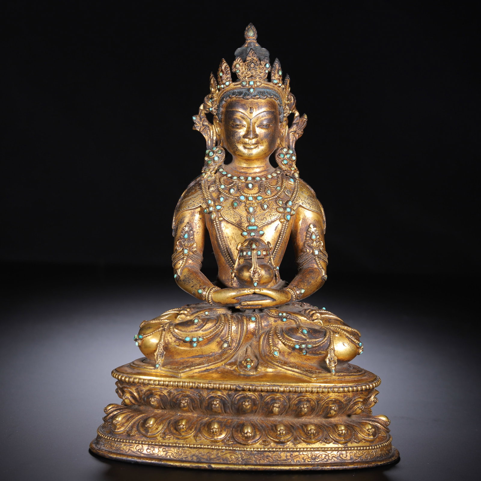 A CHINESE GILT GEM INLAID BRONZE BUDDHA: This splendid gilt bronze Buddha sits in a serene full-lotus pose atop a tiered lotus pedestal with meticulously sculpted overlapping petal rows. The ornate crown, layered necklaces, arm ornaments and