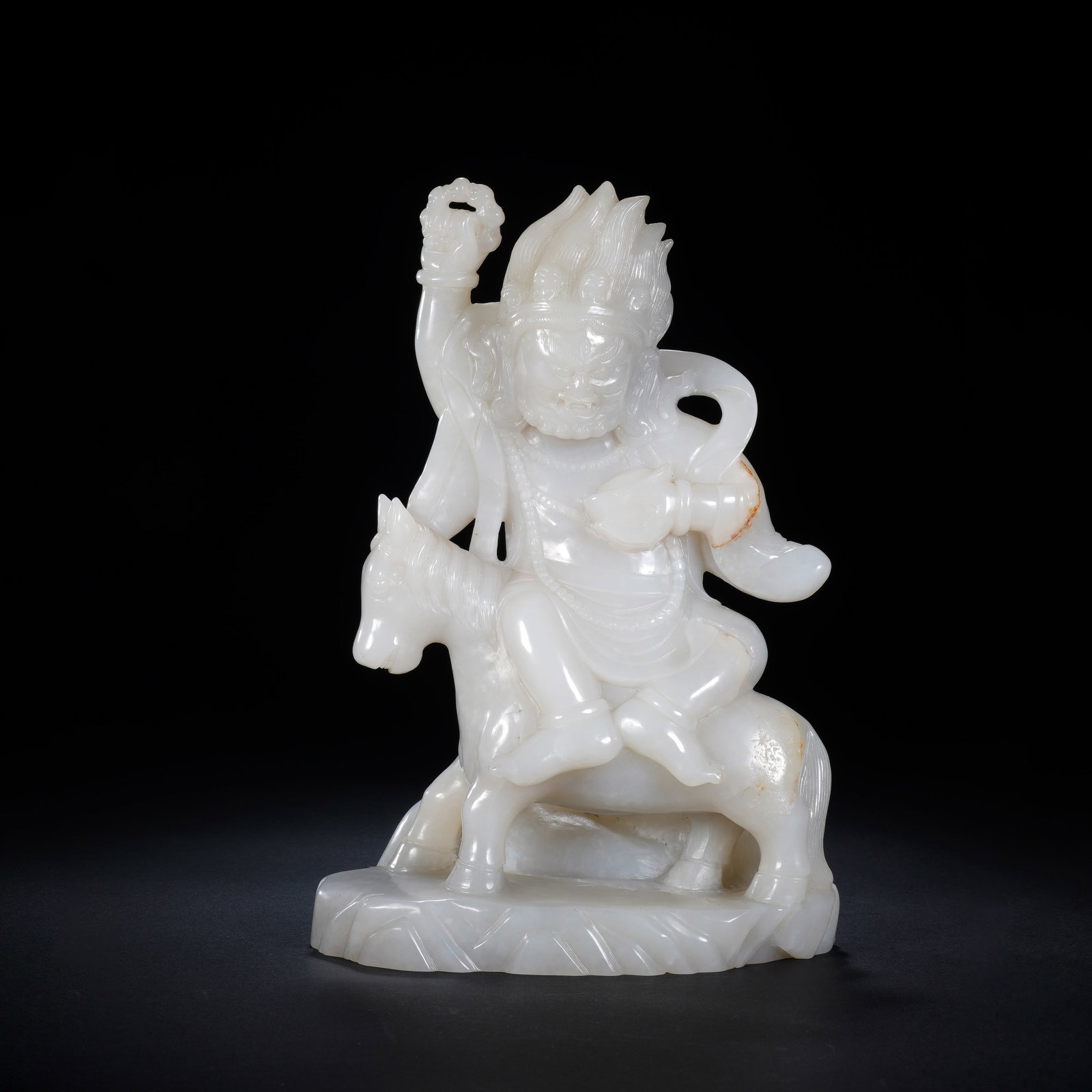A CHINESE WHITE JADE GUARDIAN DEITY FIGURE: Expertly carved from polished creamy white jade, this striking sculpture portrays a guardian deity seated firmly atop a detailed equine mount, set upon a textured rocky-style plinth. The deity feature