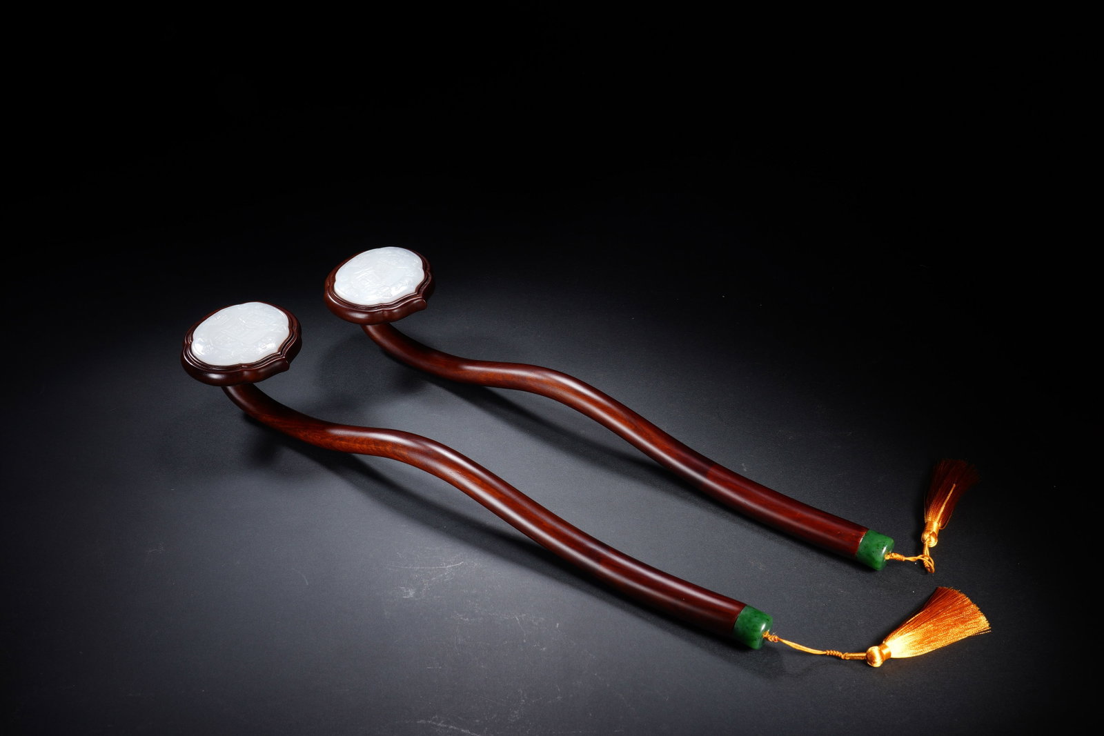 A PAIR OF CHINESE HARDWOOD INLAID JADE RUYI: This elegant matching pair of ruyi scepters is finely fashioned from polished aged hardwood, featuring gracefully undulating, smoothly contoured shafts. Each rounded ruyi head is neatly inlaid with a 