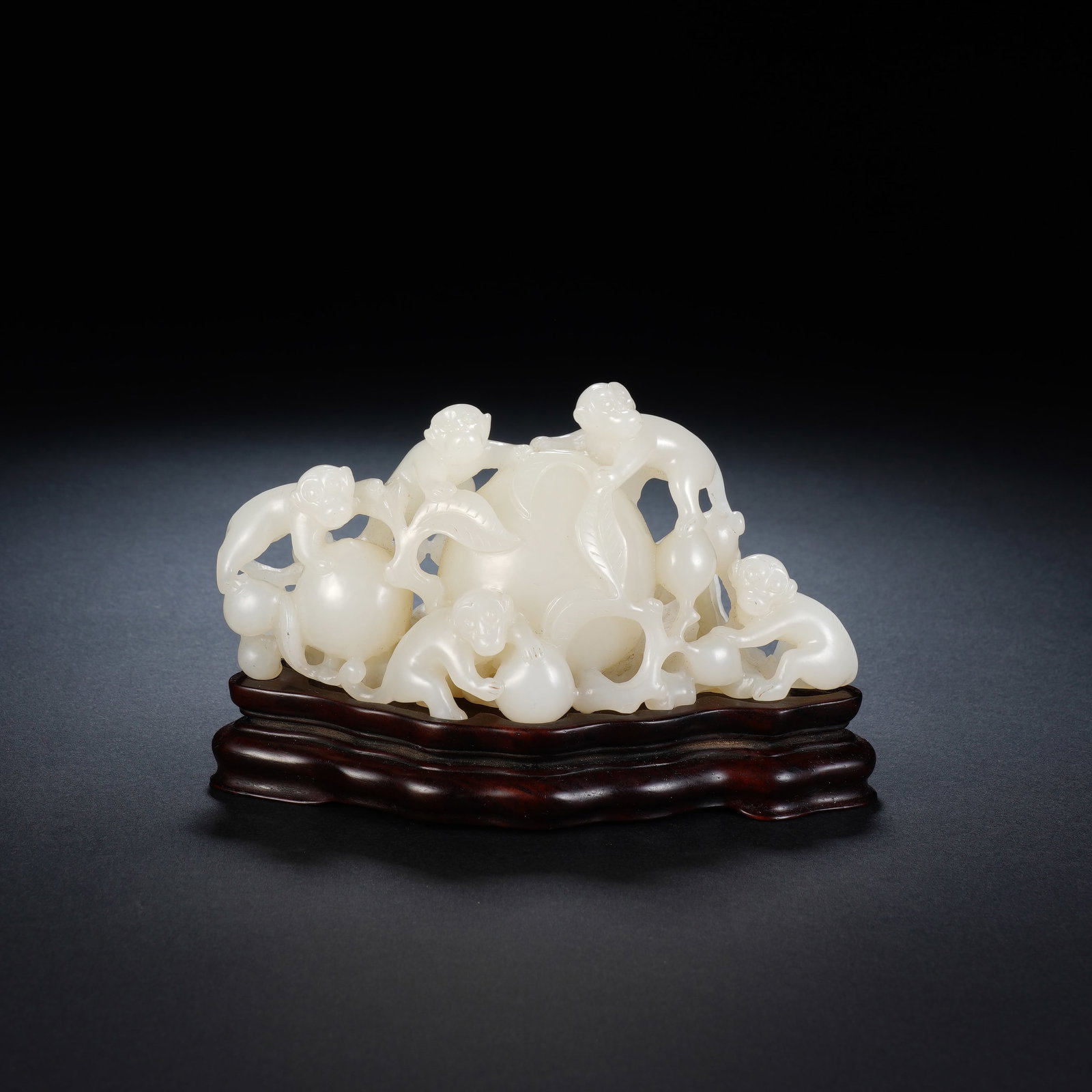 A CHINESE WHITE JADE MONKEY LONGEVITY ORNAMENT: Carved from creamy, translucent white jade, this charming ornament depicts multiple lively monkeys clambering around plump, leaf-adorned longevity peaches with fluid naturalistic detailing. Openwork c