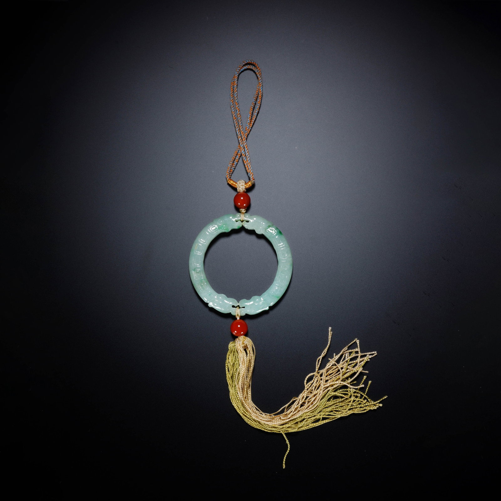 A CHINESE DRAGON PATTERN JADEITE PENDANT: Crafted from translucent pale green jadeite with soft natural tonal gradients, this circular pendant bears delicate raised dragon motifs carved along its rounded hoop. It is thoughtfully strung with t
