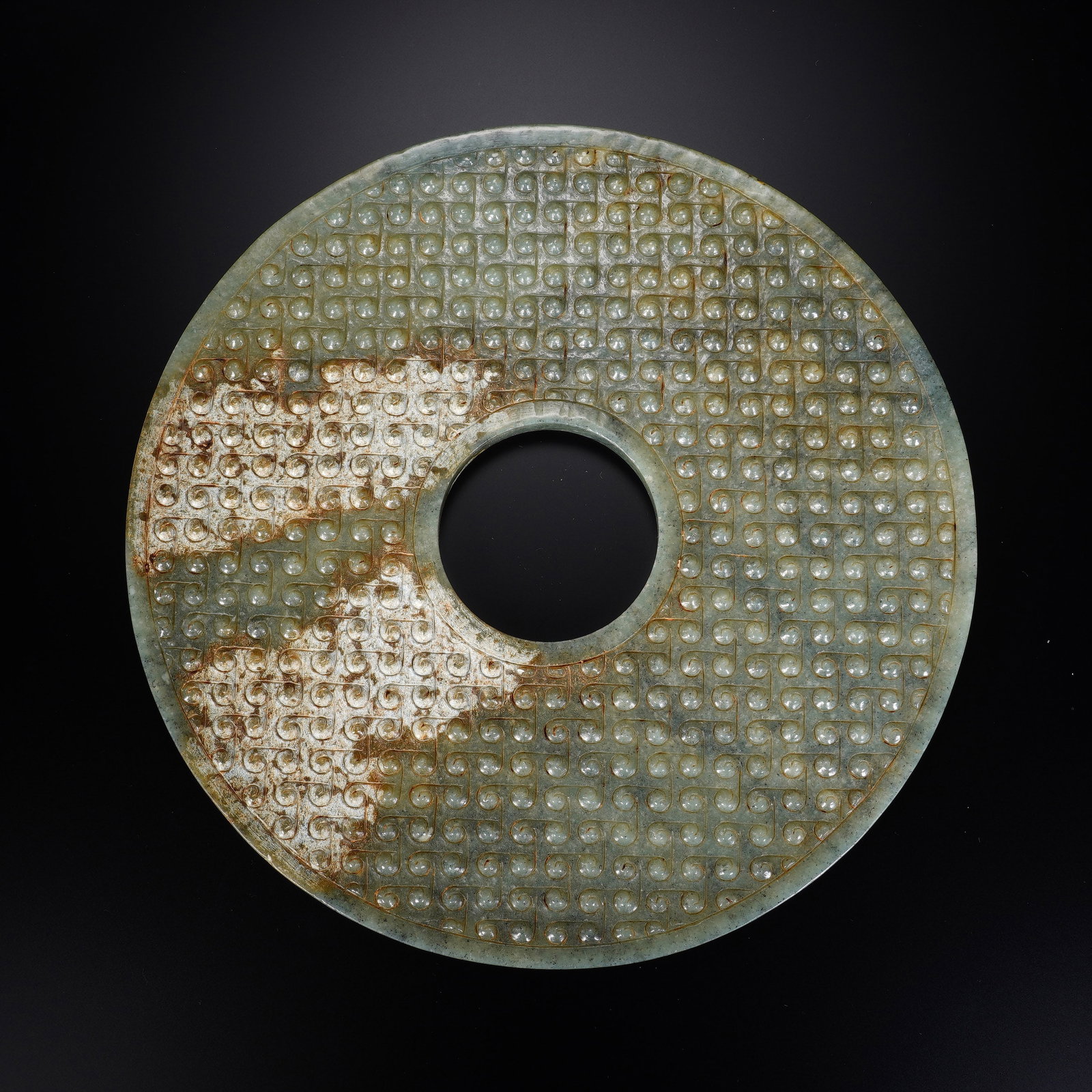 A CHINESE ANTIQUE JADE BI DISC: This substantial circular jade bi features a neatly pierced central aperture, its broad surface densely covered in orderly raised grain motifs that form a rhythmic classic decorative layout. The jade 