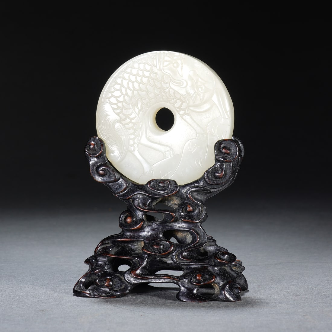 A CHINESE WHITE JADE QILIN BI WITH ZITAN STAND: The circular Hotan white jade bi has dimensions of 5 x 1.4 cm, attaining a total height of 9 cm together with its bespoke stand, and the entire assembly weighs 65 grams. The smooth milky-white jade di
