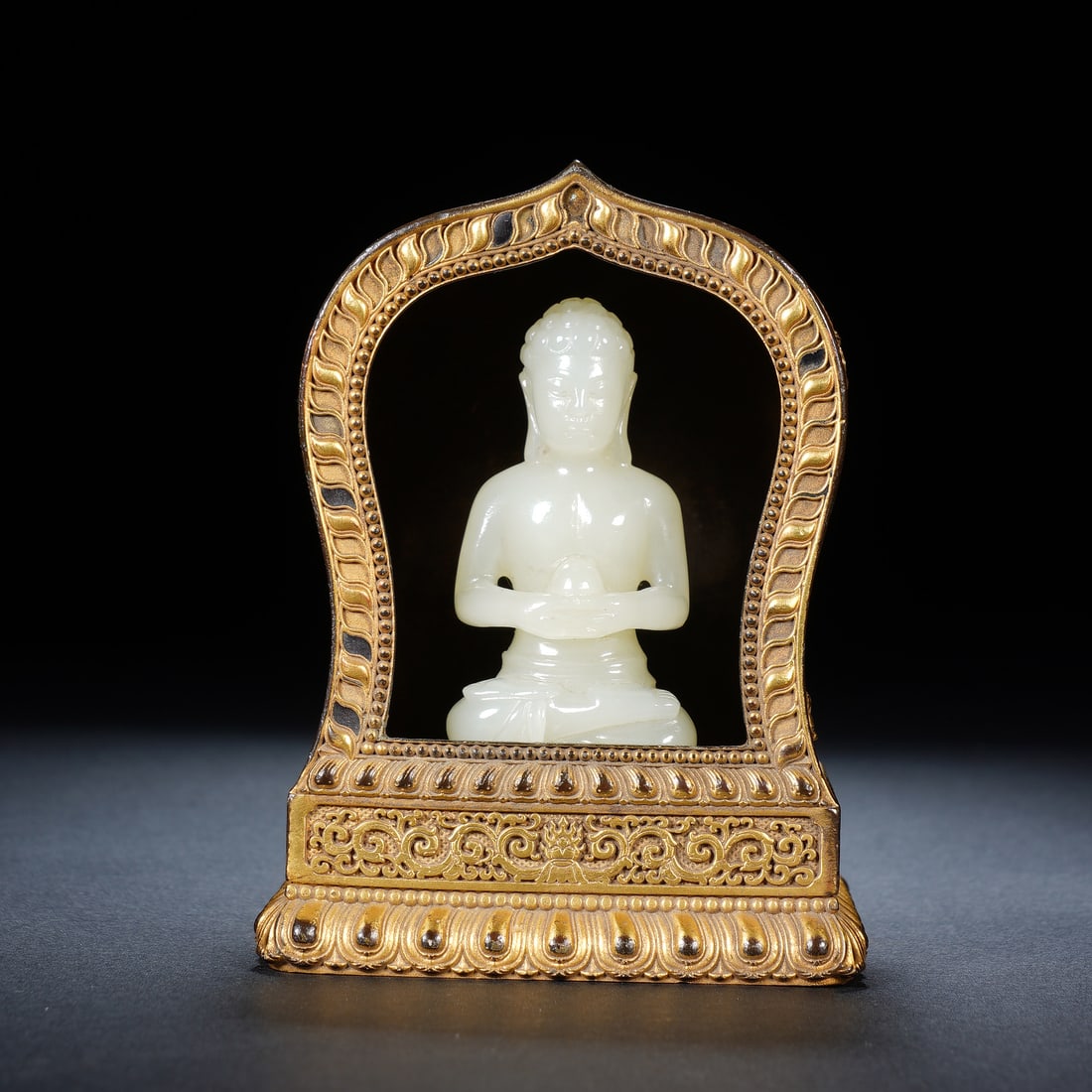 A CHINESE GILT NICHE WITH WHITE JADE BHAISAJYAGURU: Measuring 3 x 1.7 x 6 cm, the compact Hotan white jade Bhaisajyaguru sits in serene lotus posture while cradling his signature medicinal vessel. The creamy polished jade boasts a silky lustre and deli