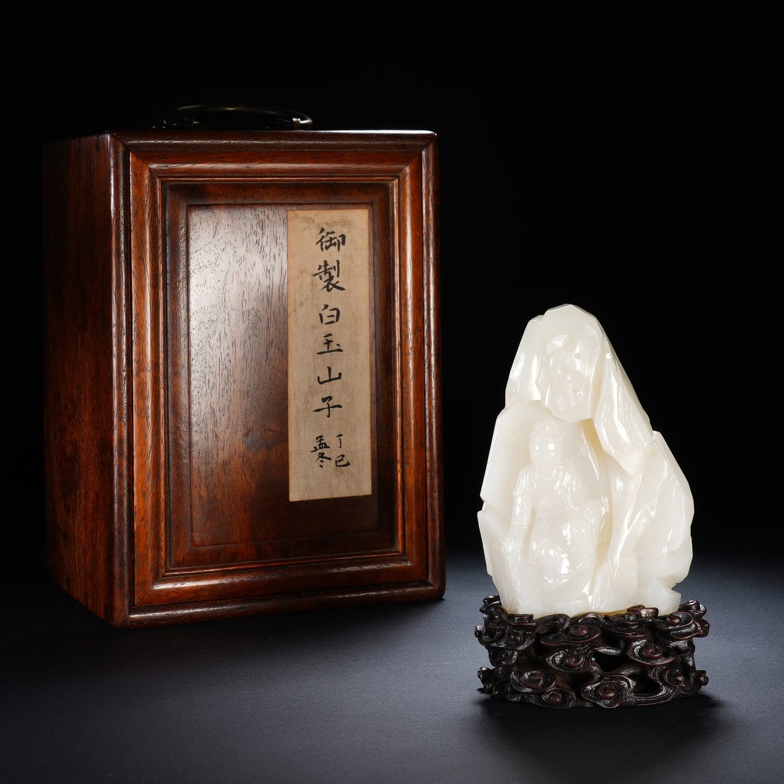A CHINESE WHITE JADE GUANYIN MOUNTAIN BOULDER: The Hotan white jade mountain boulder itself measures 8 x 4 x 11.5 cm, reaching an overall height of 14.5 cm once mounted on its carved hardwood base, with a fitted storage box sized 16 x 14 x 22 cm; 