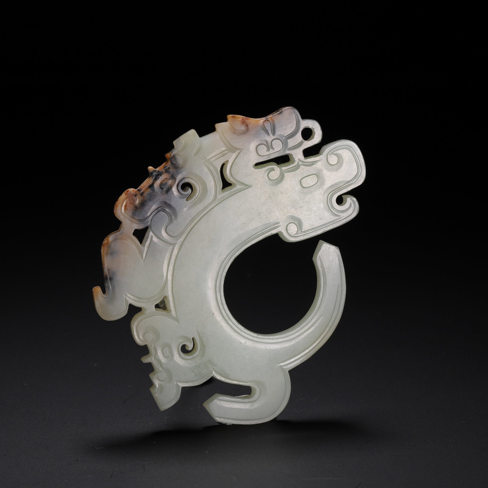 A CHINESE HETIAN JADE DRAGON BI PENDANT: Measuring 9 cm in length and 7 cm in width, this openwork Hetian jade pendant weighs 50 grams. Fashioned from pale milky nephrite, the piece takes an incomplete circular silhouette intricately carved 