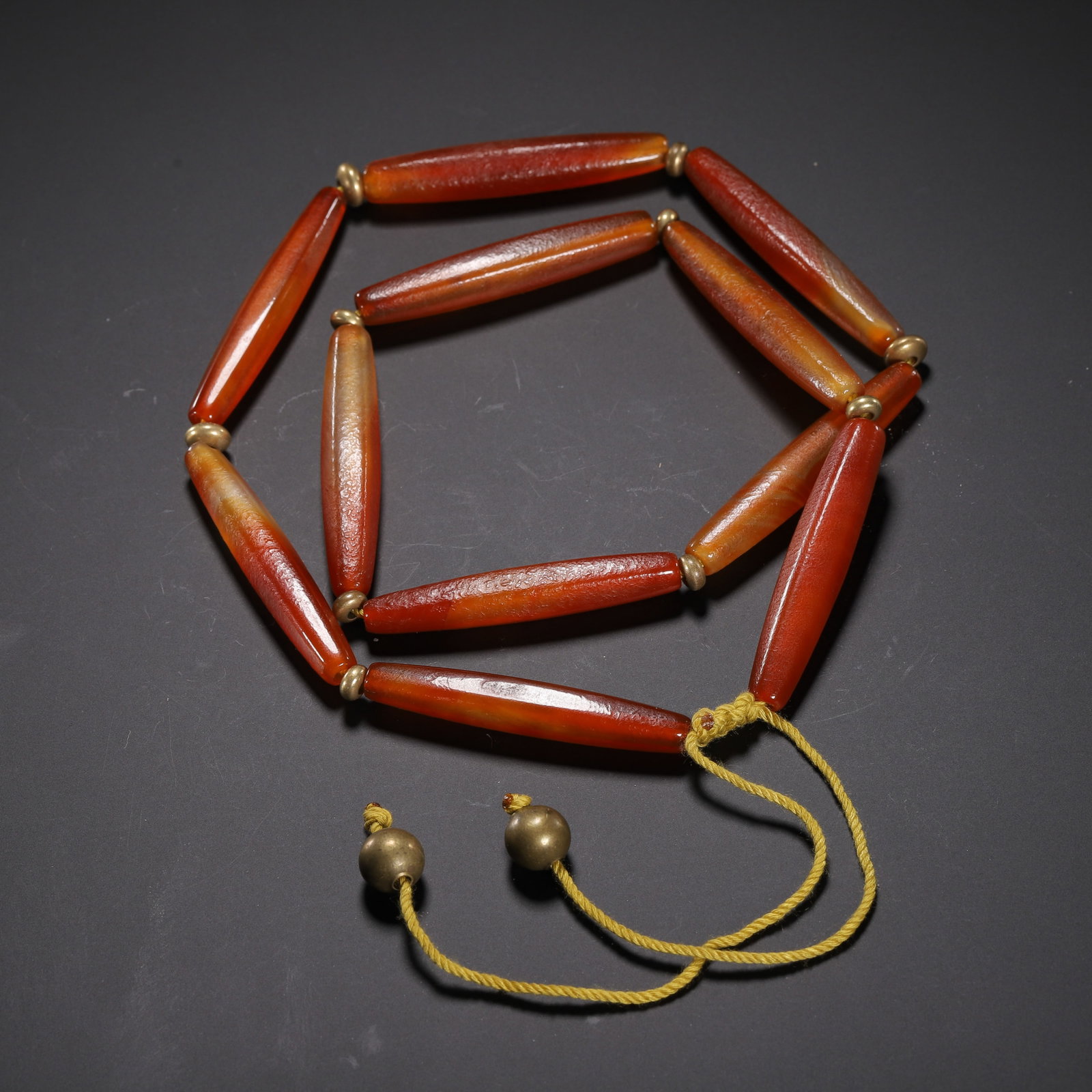A CHINESE AGATE NECKLACE: Stretching 28 cm in full length, this elegant necklace is assembled from elongated slender agate cylinders with warm layered crimson and amber tonal gradients across each bead. Tiny metallic spacer be