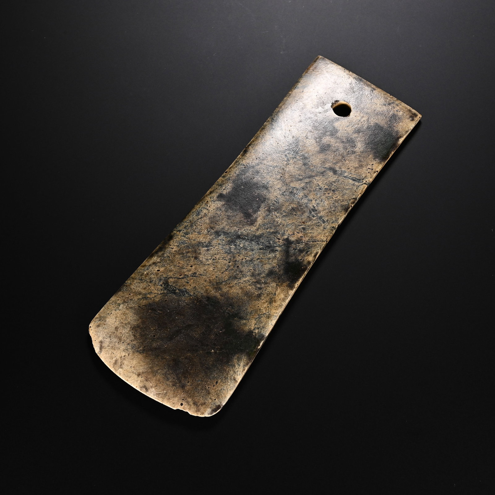 A CHINESE HETIAN JADE RITUAL TABLET: Measuring 17.2 cm in length and 6.7 cm in width, this elongated flat Hetian jade implement features a smoothly curved distal blade edge and a neatly drilled circular perforation near the narrower