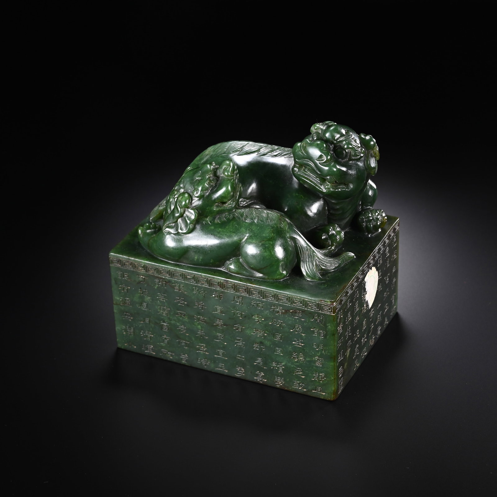 A CHINESE HETIAN JASPER SEAL: Standing 10 cm in height and 10.5 cm in width, this substantial square seal is carved from rich deep-green Hetian jasper with a sleek, lustrous polish. Its apex showcases an elaborate knob featuring