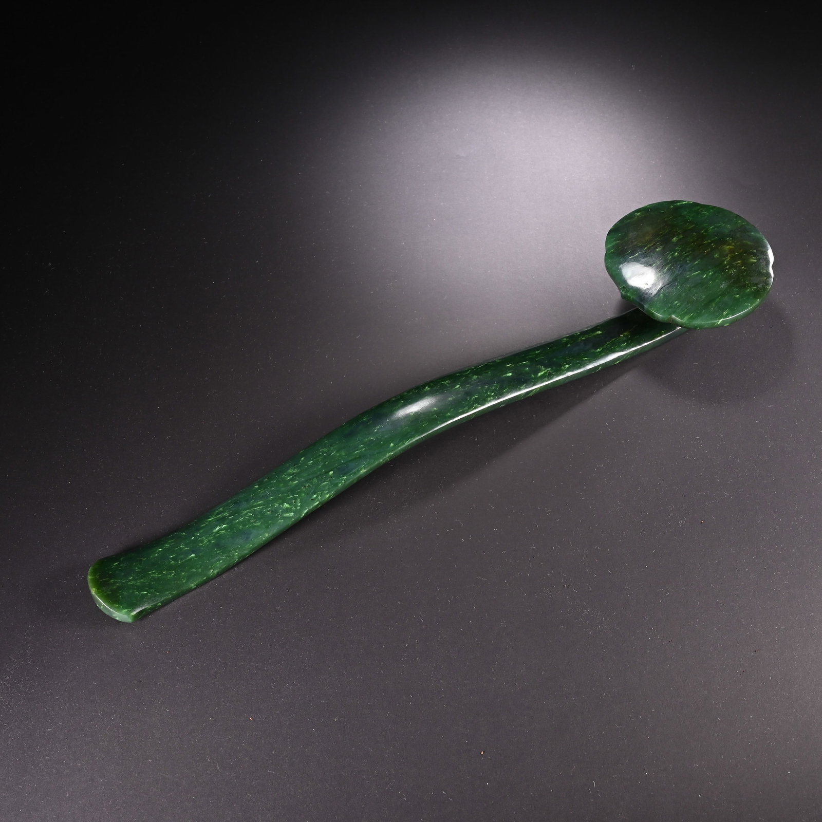 A CHINESE HETIAN JASPER RUYI: Measuring 35.5 cm in length and 8.5 cm in width, this elegant sceptre is carved from deep-green Hetian jasper marked by natural subtle mottled inclusions across its glossy polished exterior. It