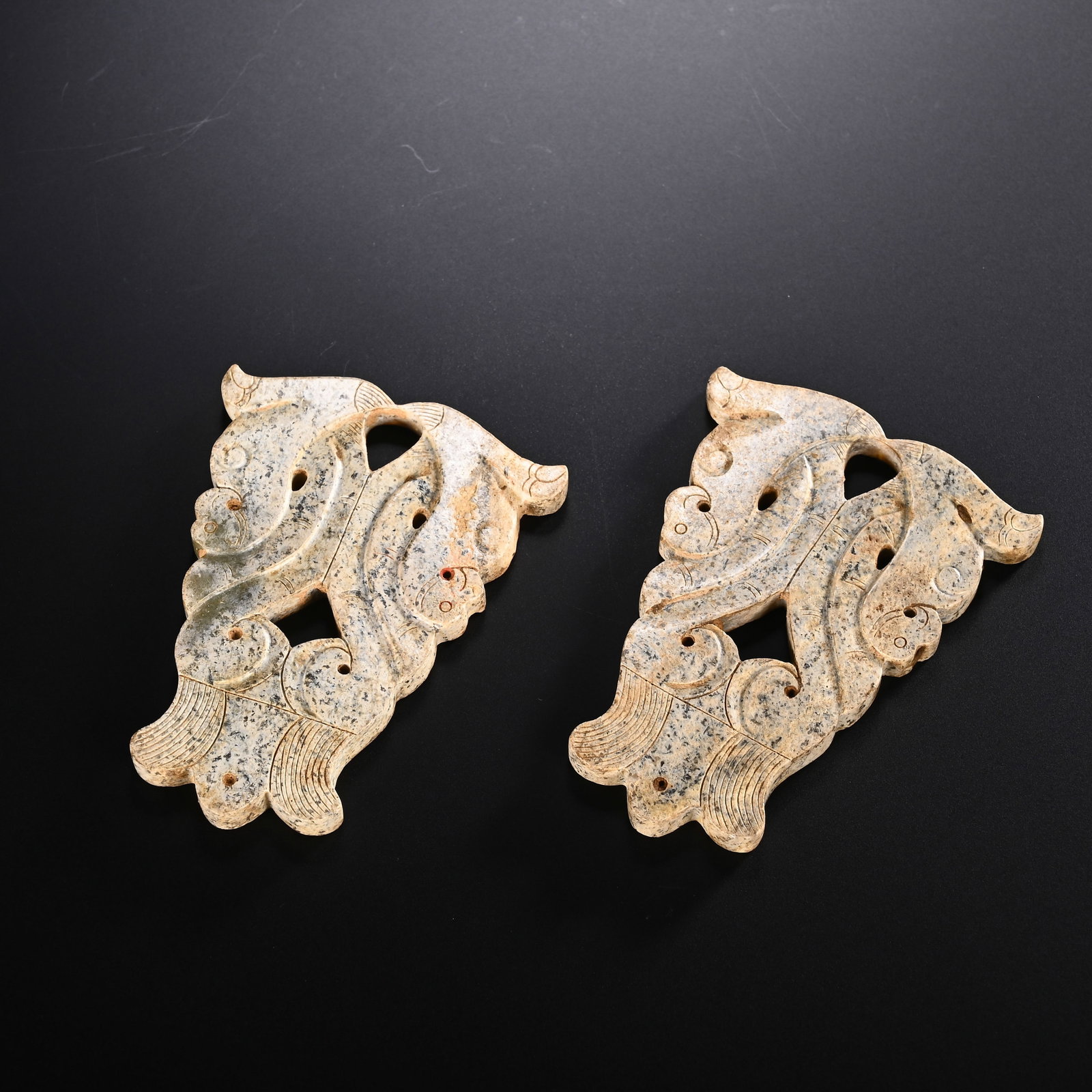 A PAIR OF CHINESE OPENWORK JADE ORNAMENTS: This matched pair of jade ornaments features graceful openwork carvings fashioned into elegant archaic stylized motifs. The natural jade displays attractive mottled speckled patina alongside warm beig