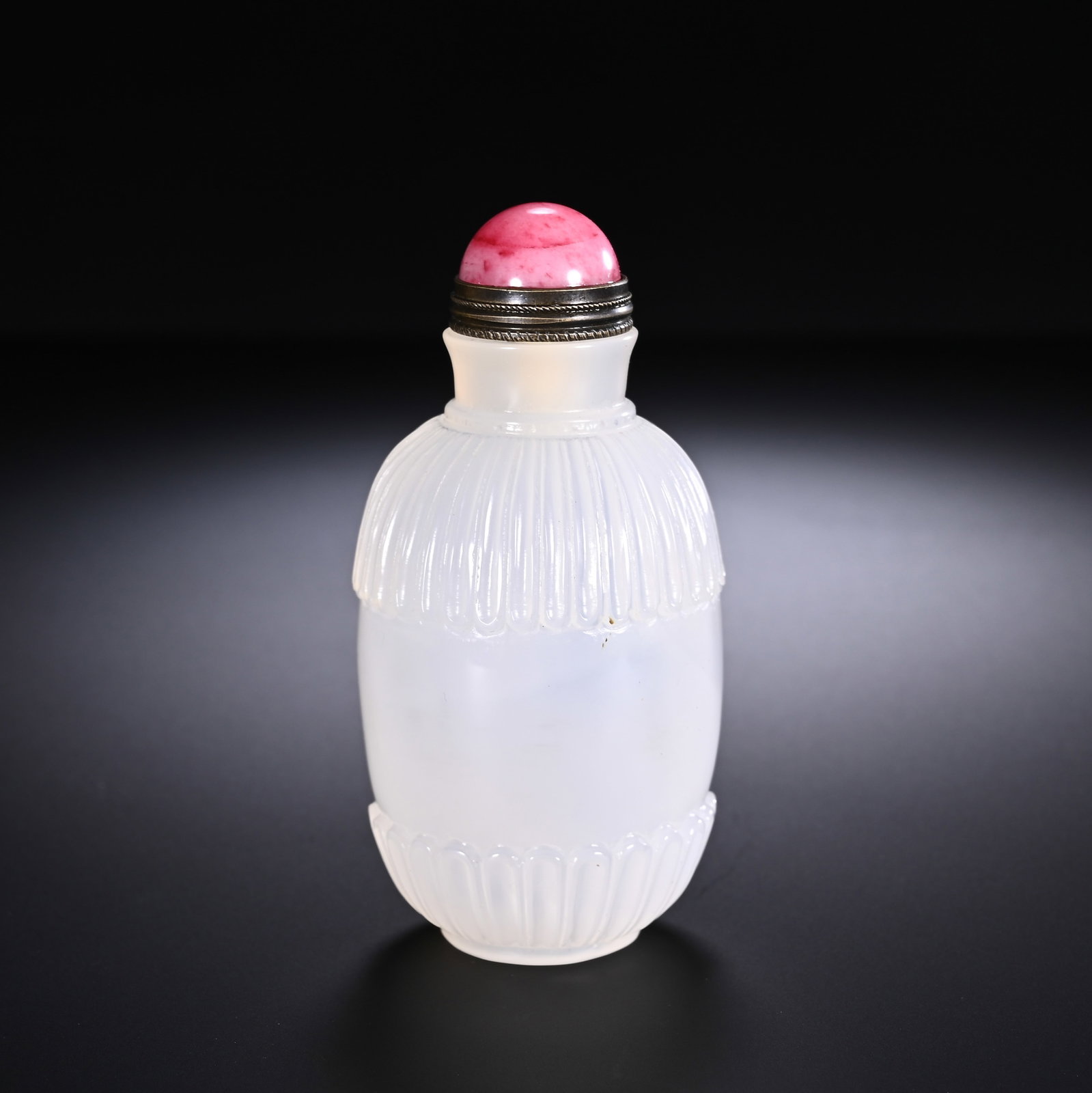 A CHINESE AGATE SNUFF BOTTLE: Carved from pale, milky translucent agate, this elegant snuff bottle boasts a streamlined rounded silhouette. Neatly rendered fluted petal patterns adorn both the shoulder and foot of the vessel, crea