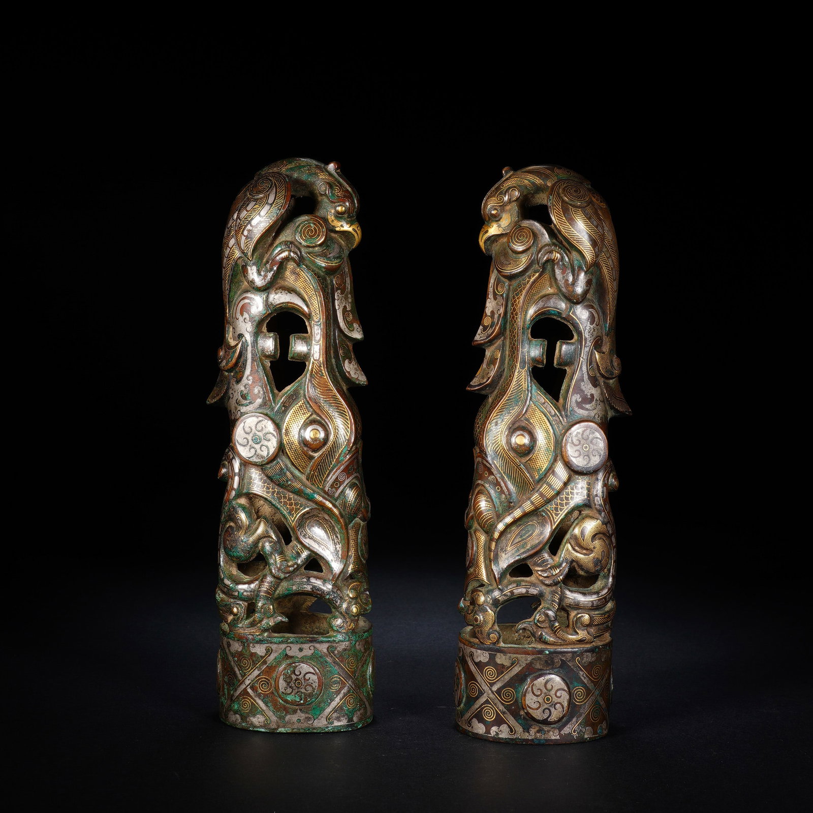 A PAIR OF CHINESE GOLD SILVER INLAID BRONZES: This harmoniously matched pair of tall bronze fittings boasts elaborate openwork carvings with avian motifs crowning the upper section, intertwined with curling mythical creatures along the cylindrica