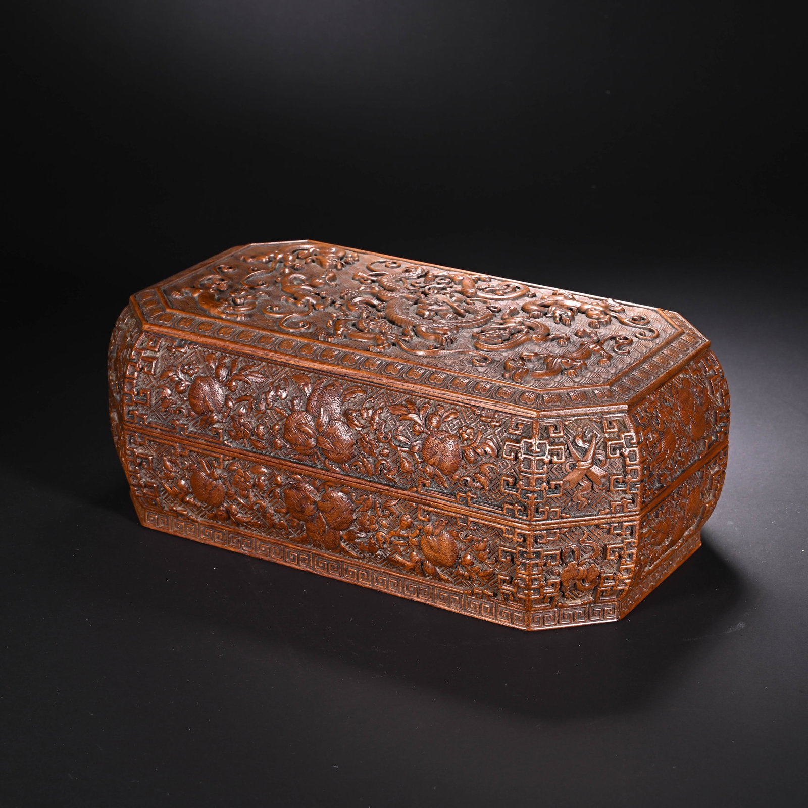 A CHINESE HUANGHUALI DRAGON PATTERN BOX: Standing 9.5 cm tall and 25 cm wide, this octagonal lidded box is masterfully fashioned from premium huanghuali timber displaying warm natural wood grain and a soft aged patina. Deep-relief carvings d