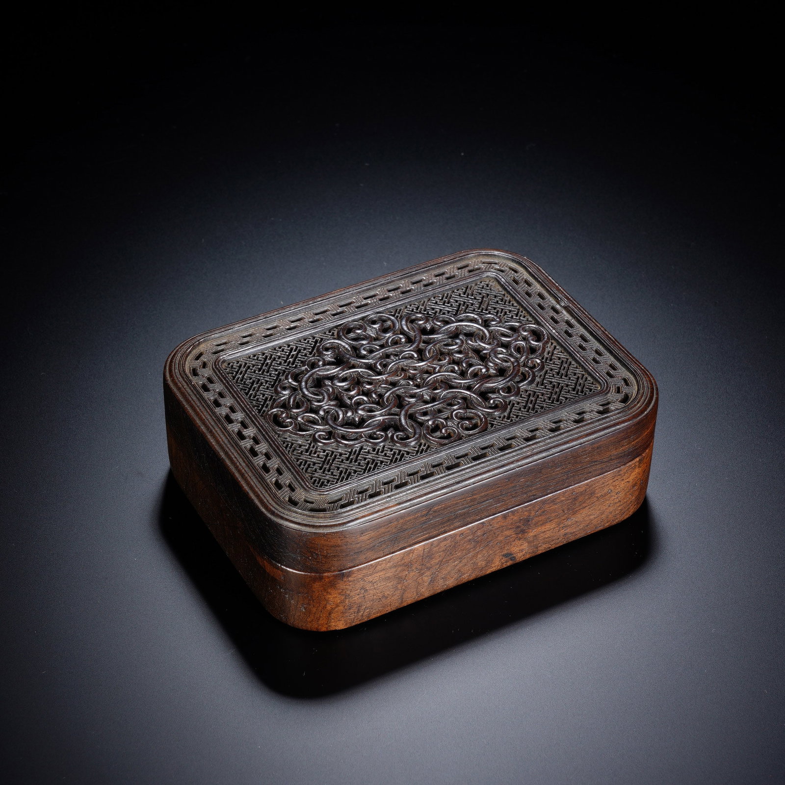 A CHINESE OPENWORK ZITAN INCENSE BOX: Crafted from premium zitan hardwood with naturally warm, varied wood grain on its smooth rectangular casing, this compact incense box features rounded corners for elegant softness. The lid showcases e