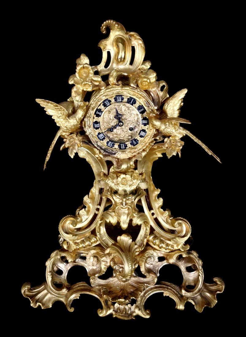 Gilt Bronze French Clock, Marti: A large Louis XV Rococo style gilt bronze mantle clock with gilt and ebonized face framed by two large figural birds, supported on an elaborate, openwork scrolled frame with central satyr mask, c-scro