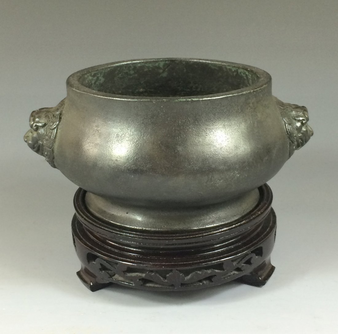 AN ANTIQUE BRONZE CENSER W/ STAND: An Antique Chinese Bronze Censer With Stand. Globular body, with flared flat foot base, Two Foo-Lion mask flanked on the body below the rim. Displayed upon a carved hardwood base. Mark on base, incise