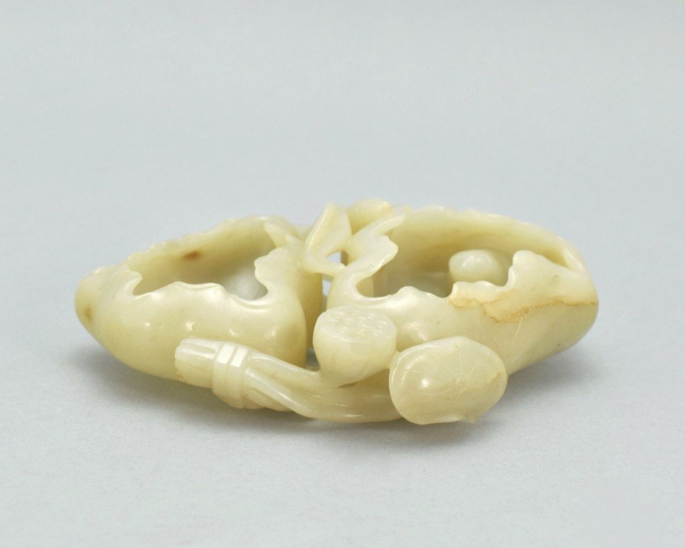 JADE BRUSH WASHER IN SHAPE OF LOTUS LEAFS AND PODS: The nephrite jade carved to recumbent conjugated lotus leafs, both curved to a deep bowl shape, with lotus seed pod and stems overlaid from the base. The jade shows creme-grayish iridescent, with spor