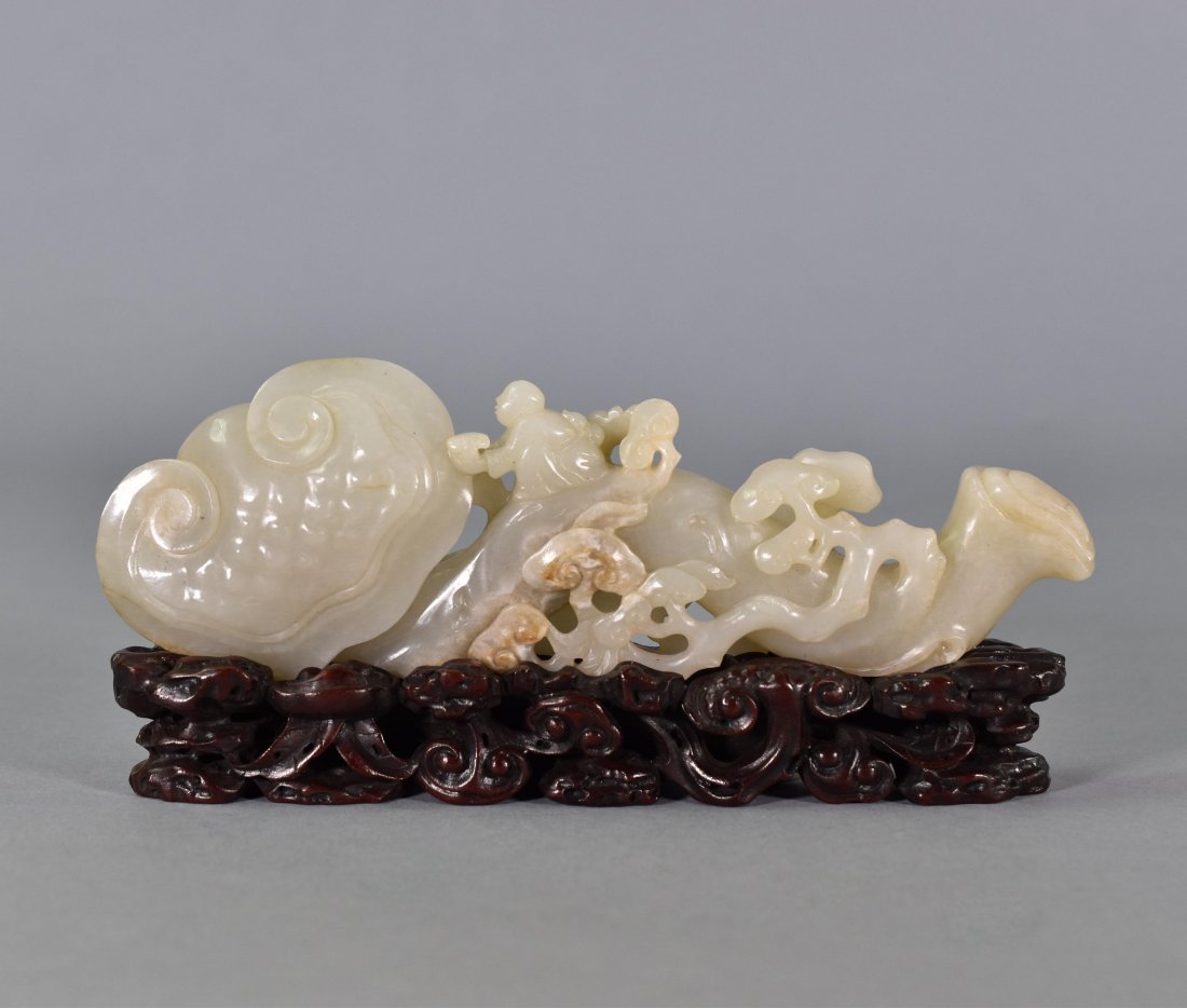 CARVED JADE OF BOY RIDES RUYI: The jade carved into a shape of a boy riding a wish-granting-wand ruyi scepter, the boys seated on the wand next to the ruyi head, the arched and curved wand surmounted elaborately open-work carved st