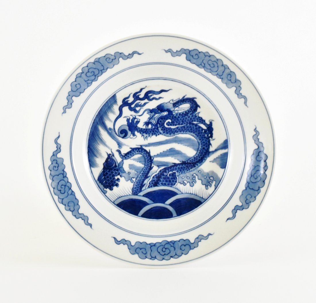 BLUE AND WHITE DRAGON PLATE, KANGXI MARK: Potted with shallow rim body, the central interior decorated in cobalt blue glaze of vigorous dragon soaring within turbulent cresting waves chasing a flame pearl next to a leaping fish. Scrolling clo