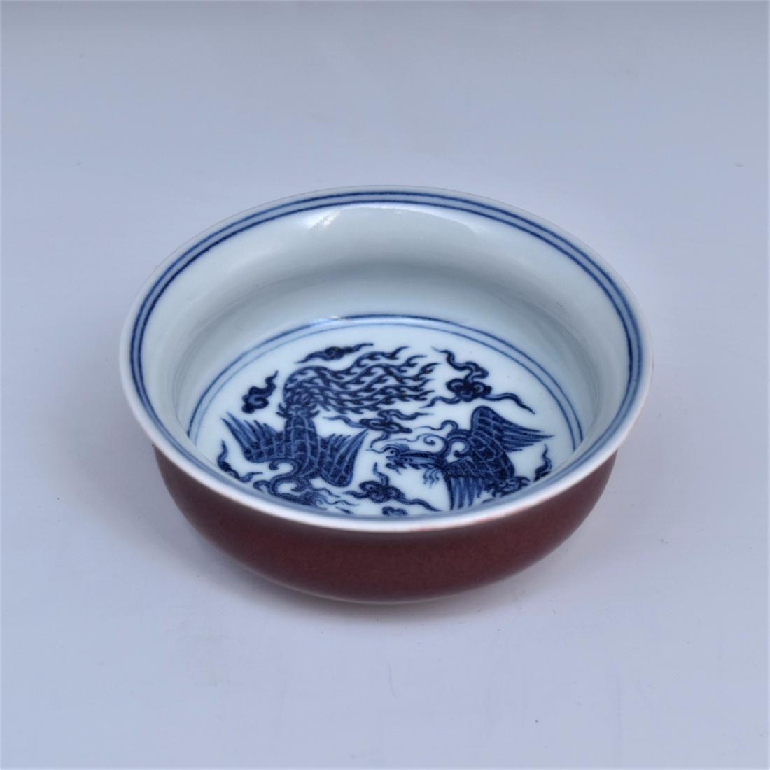 BLUE AND WHITE PHOENIX MOTIF ON RED BOWL: Potted in shallow vessel, flat broad cavetto rising the steep sides toward slightly flared rim, supported upon fitted base. The central interior hand painted in cobalt-blue underglazed with two phoeni