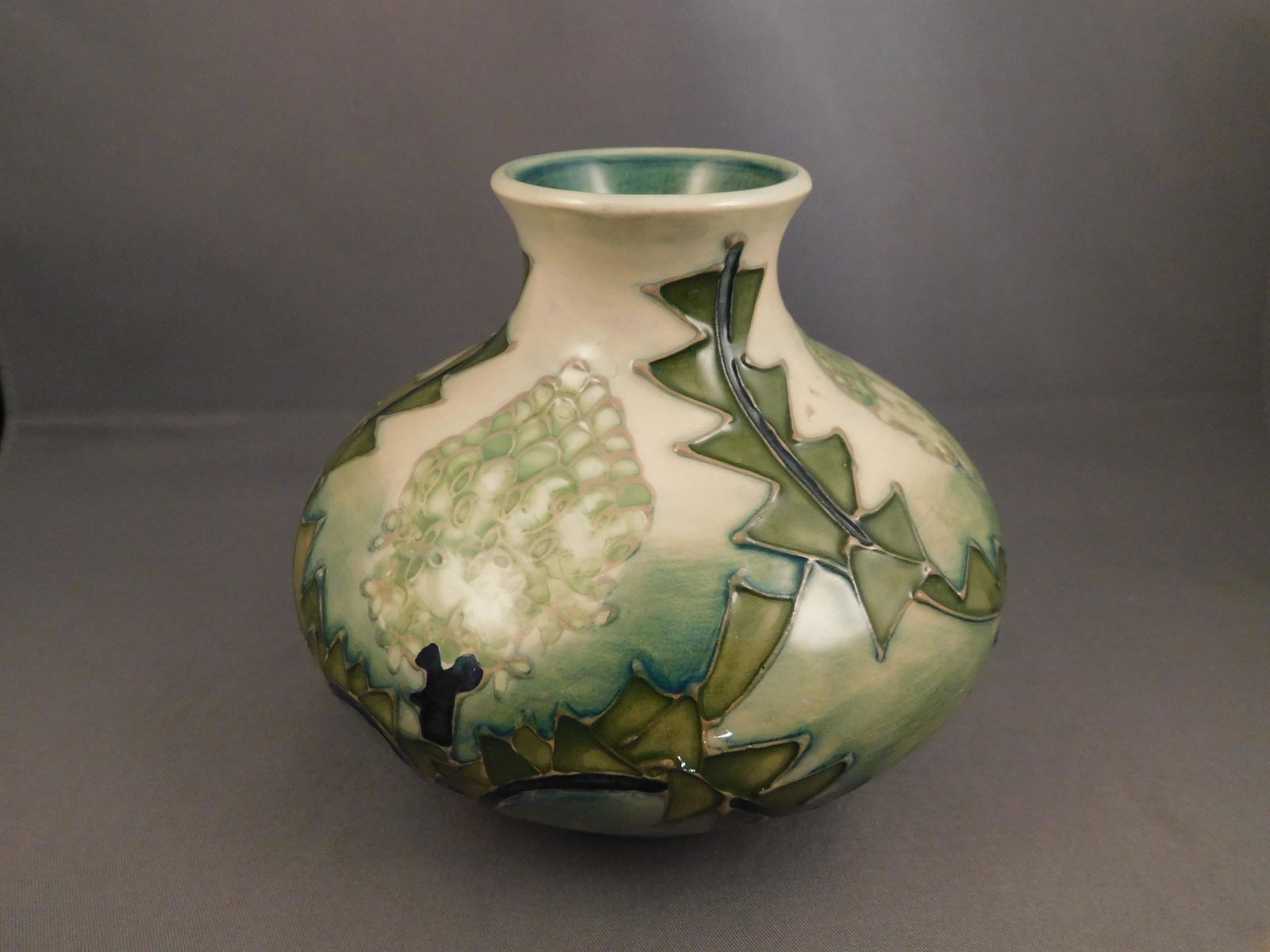 Moororoft Vase: Moororoft art pottery vase with a green tree/leaf pattern and a glaze finish. Measures approx. 4 1/4" tall x 5 1/2" wide. You are bidding at a live sale. Please read the terms and conditions. We are o