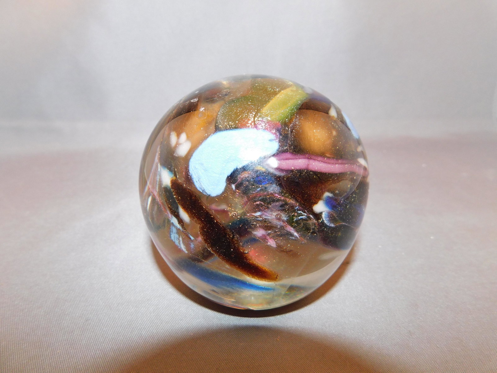 ASTP Art Glass Paperweight: ASTP art glass paperweight with a gold specked and multi colored interior. Measures approx. 2 3/4" tall x 2 3/4" wide. You are bidding at a live sale. Please read the terms and conditions. We are offe