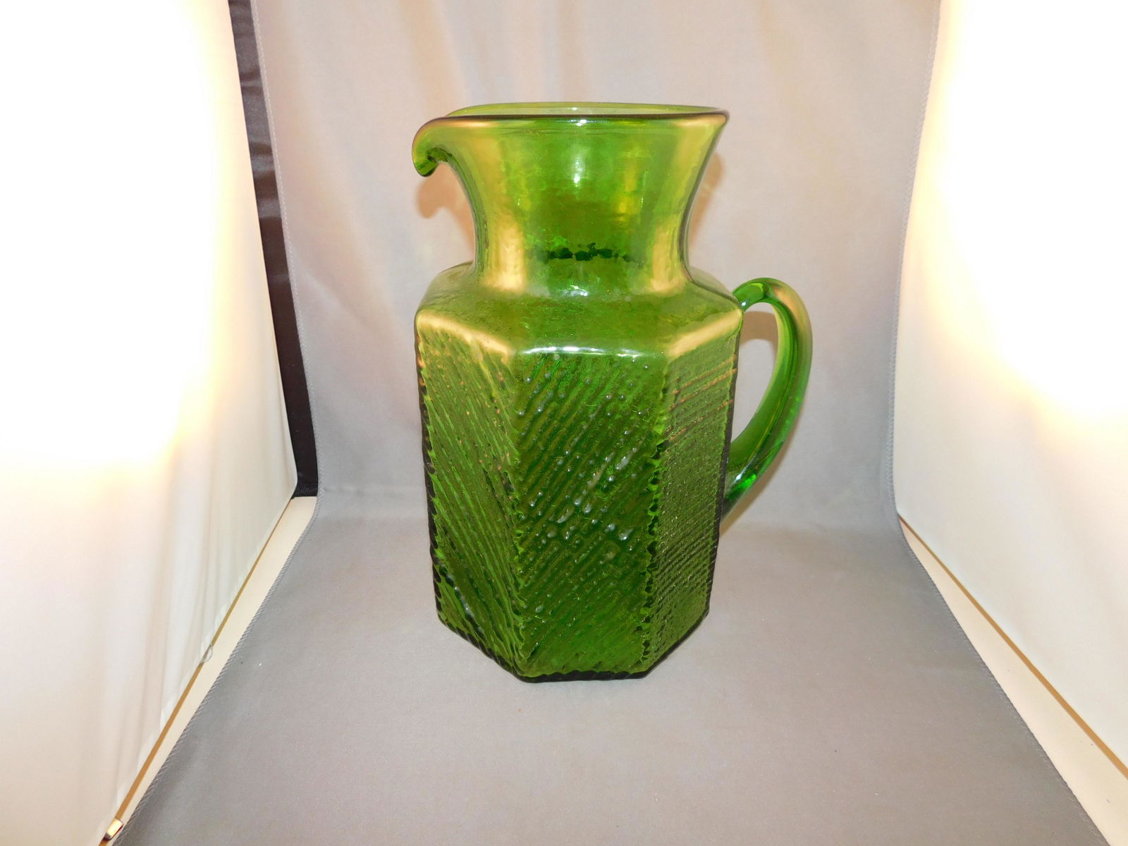 Art Glass Pitcher: Art glass pitcher in a green modern style. Possibly Blenko. Measures approx. 10 1/4" tall x 7 1/2" wide. You are bidding at a live sale. Please read the terms and conditions. We are offering no contac