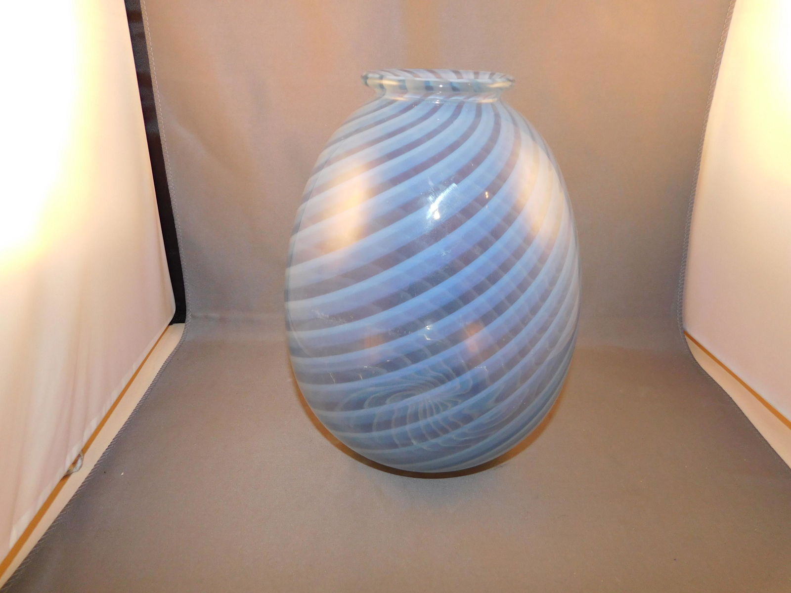 Art Glass Vase: Blue art glass vase in a blue swirl. Measures approx. 8" tall x 5 1/2" wide. You are bidding at a live sale. Please read the terms and conditions. We are offering no contact pick up at our South Bruns