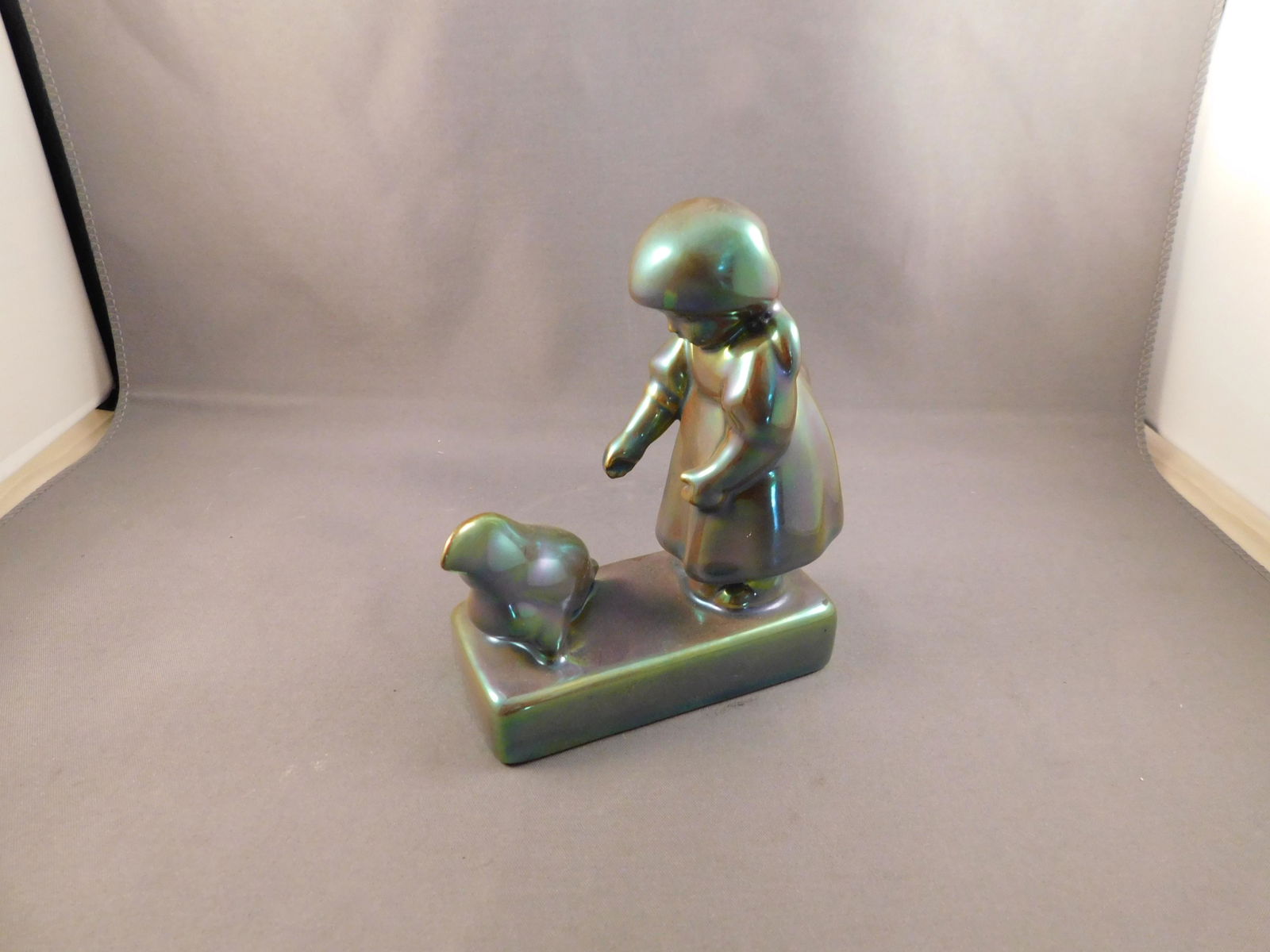 Zsolnay Girl: Zsolnay blue/green iridescent girl with chicken. Measures approx. 4 1/2" tall x 3 1/2" wide. You are bidding at a live sale. Please read the terms and conditions. We are offering no contact pick up at
