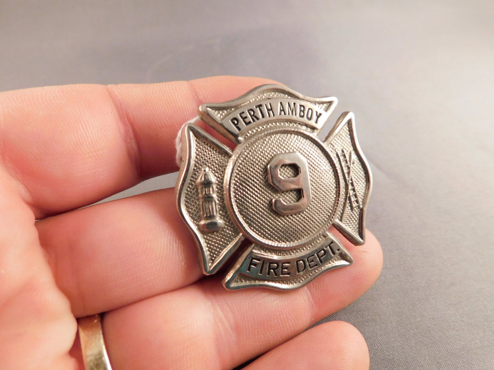 Perth Amboy Fire Badge: Silver tone Perth Amboy Fire Dept badge with 9 in the center. Measures approx. 1 3/4" long. You are bidding at a live sale, please read the terms and conditions. We are offering contact-less pick ups 
